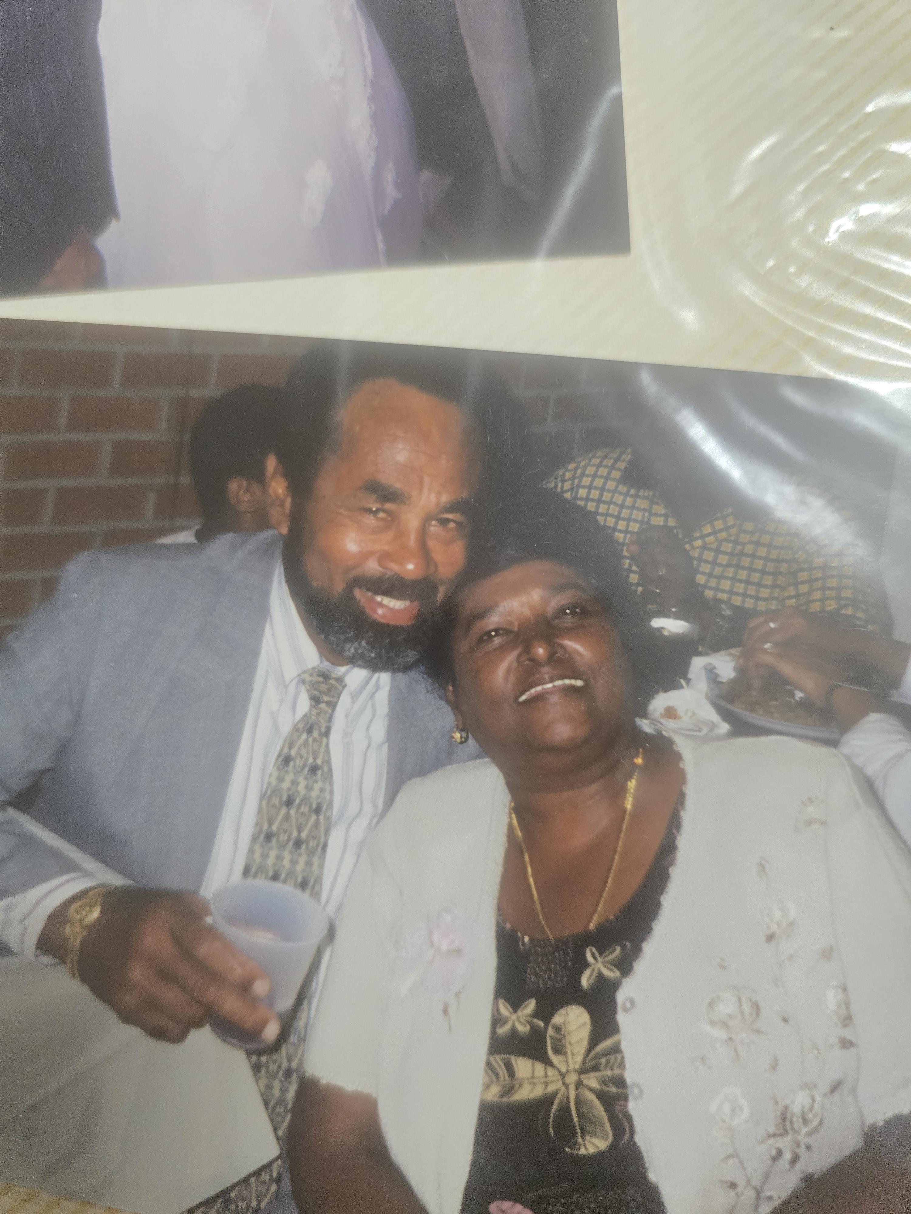 A couple enjoys a warm embrace, smiling happily at a family gathering during the evening.