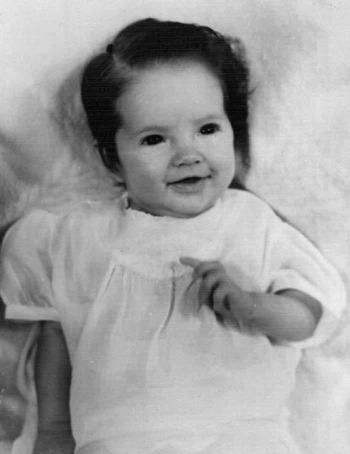 A baby with a joyful smile lounges comfortably on a fluffy surface, exuding innocence.