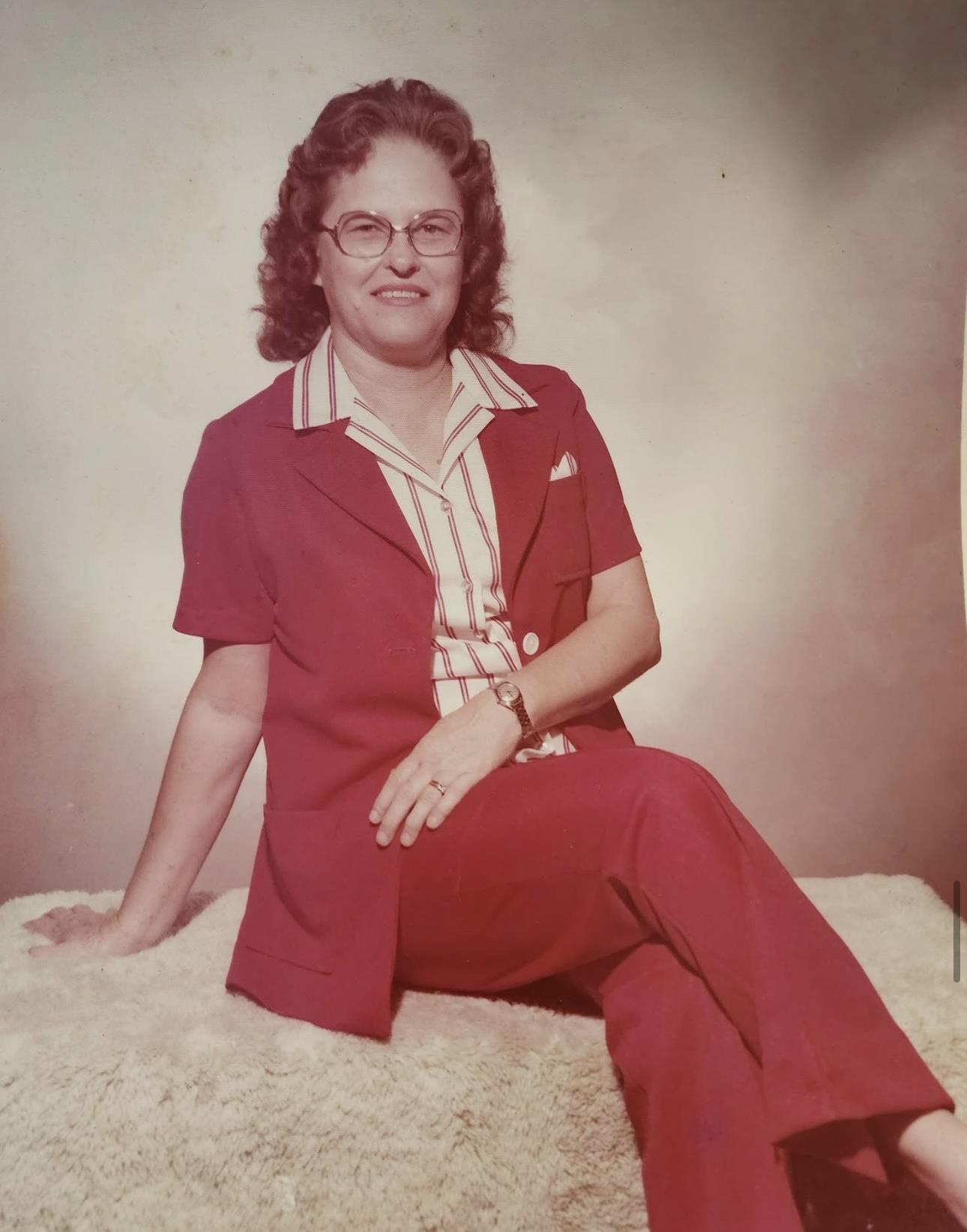 Person wearing a striking red suit with a striped shirt sits confidently on a stone backdrop.