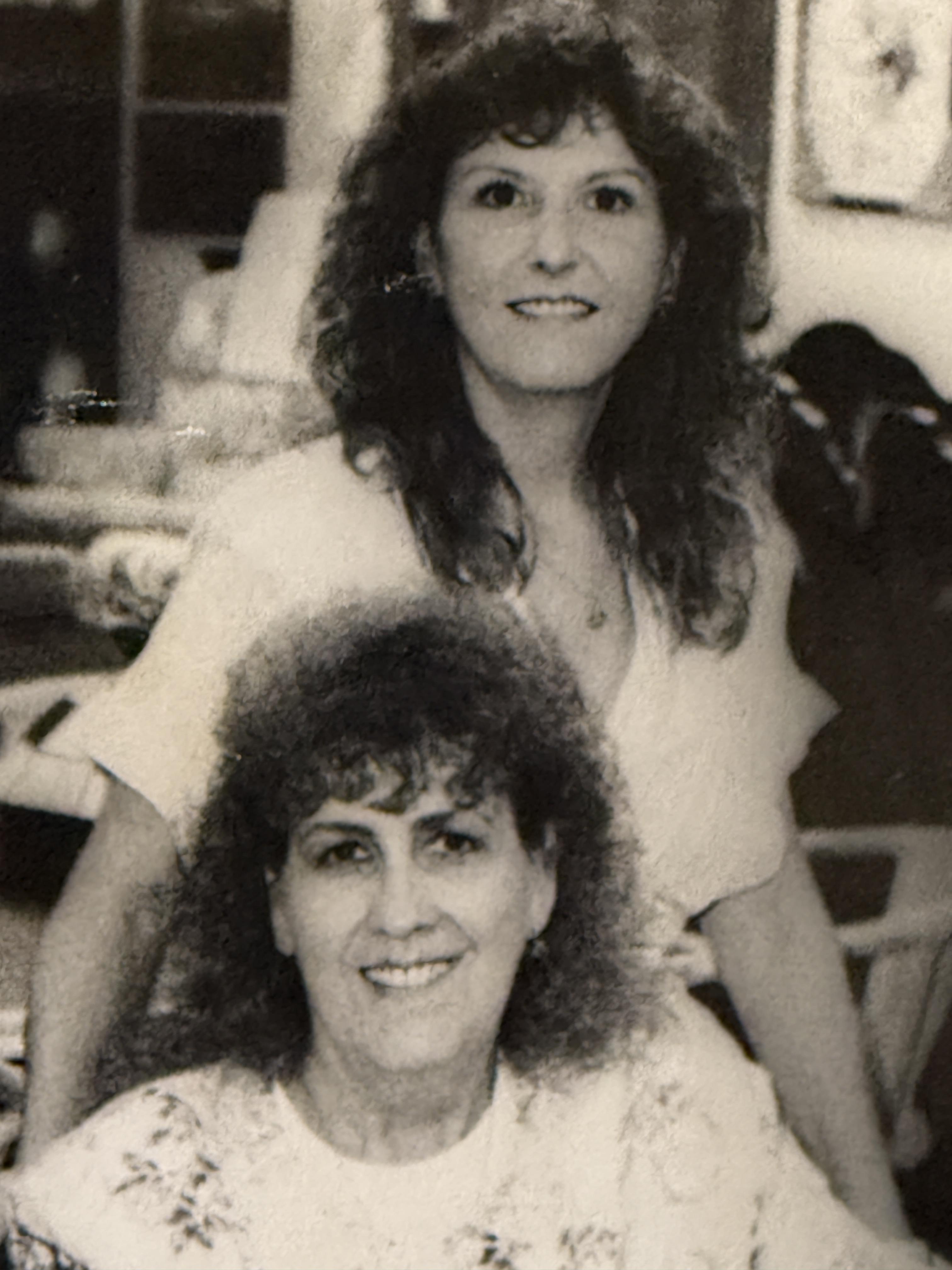Two women with curly hair are posing happily in a warm, inviting indoor environment.