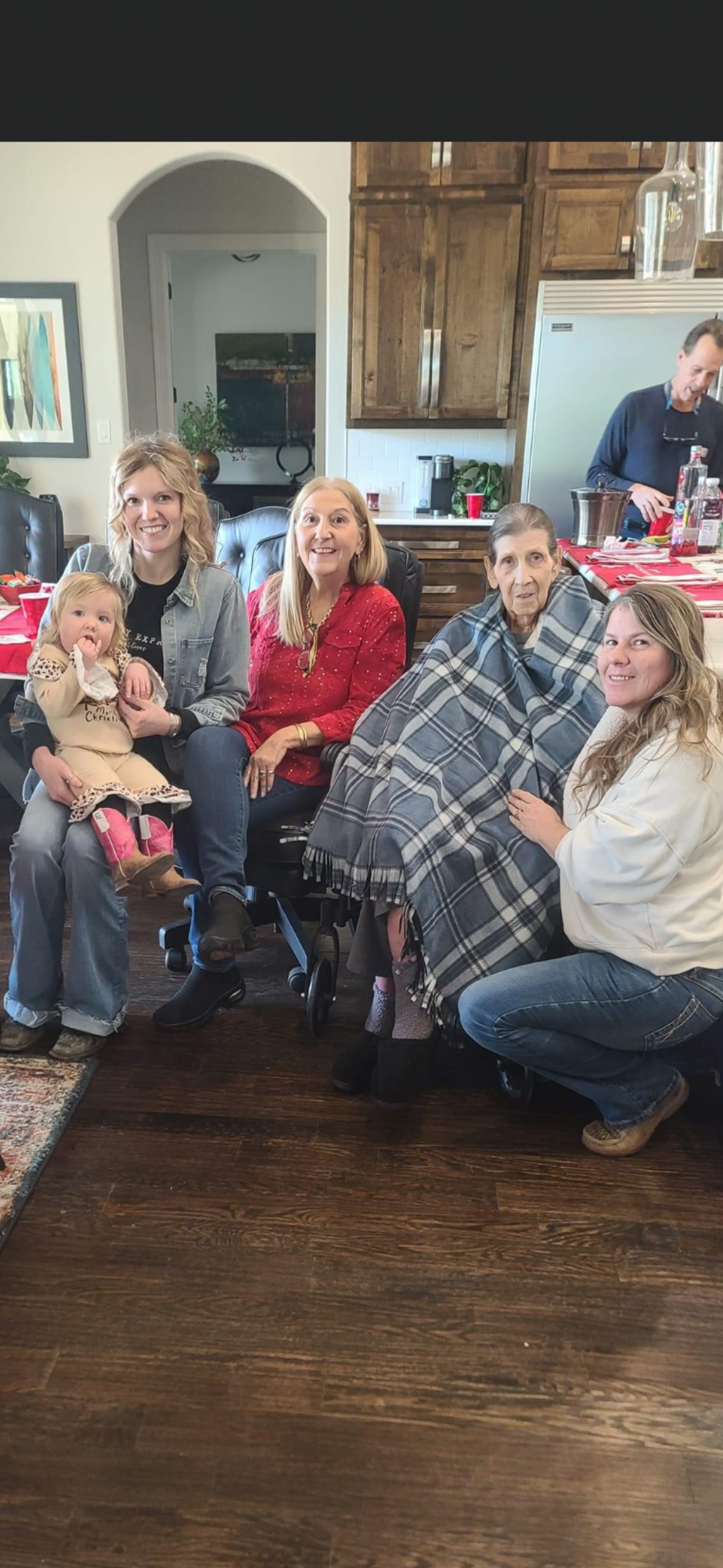 Four women and a young girl are gathered together in a warm home, smiling and interacting.
