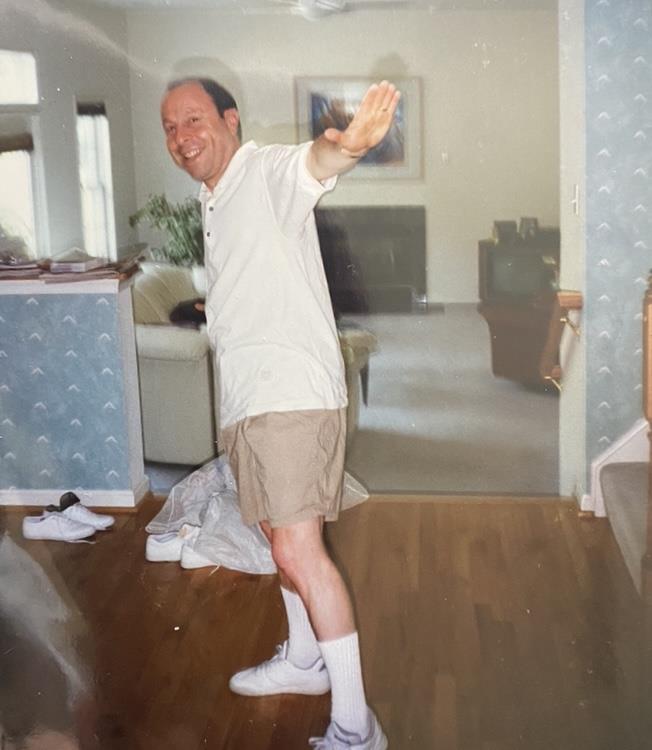 A man is dancing joyfully in his home while wearing shorts and a casual shirt.