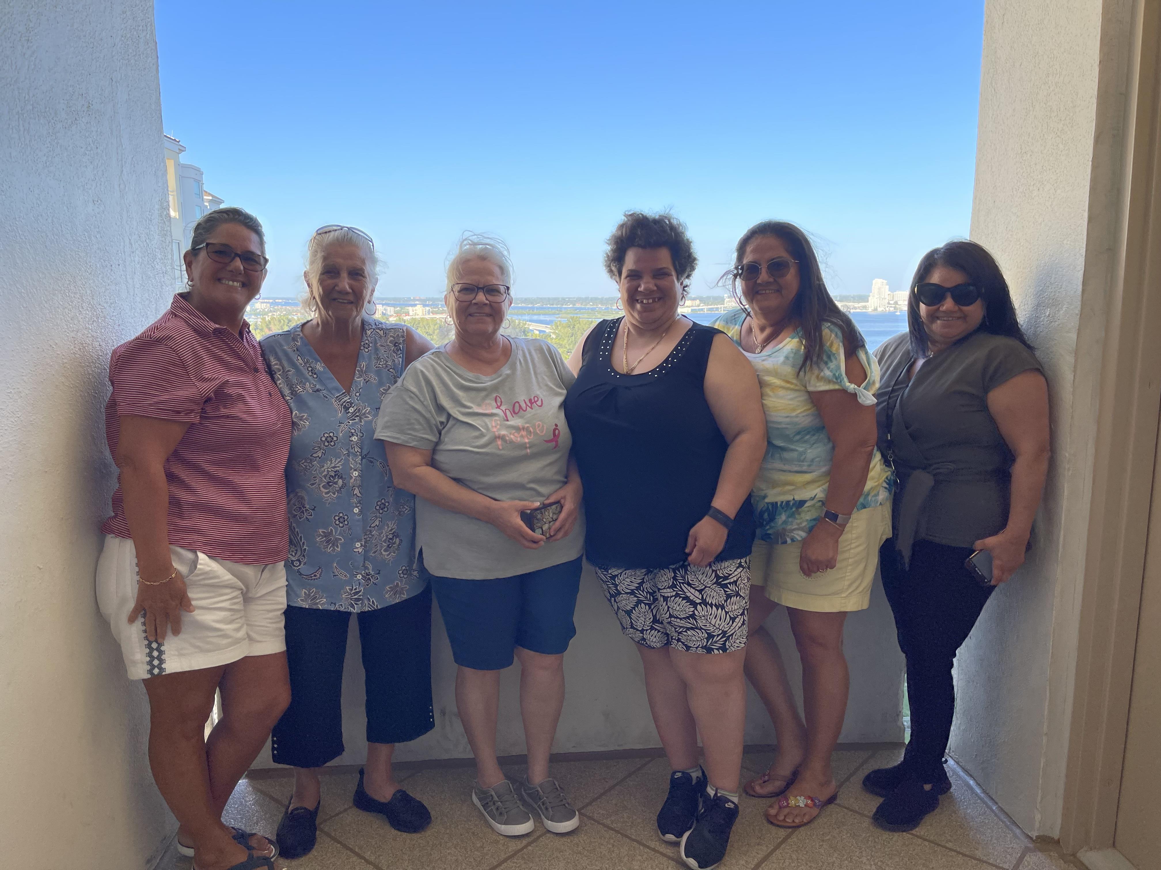 A cheerful gathering of friends on a balcony overlooking the ocean on a bright, sunny day.