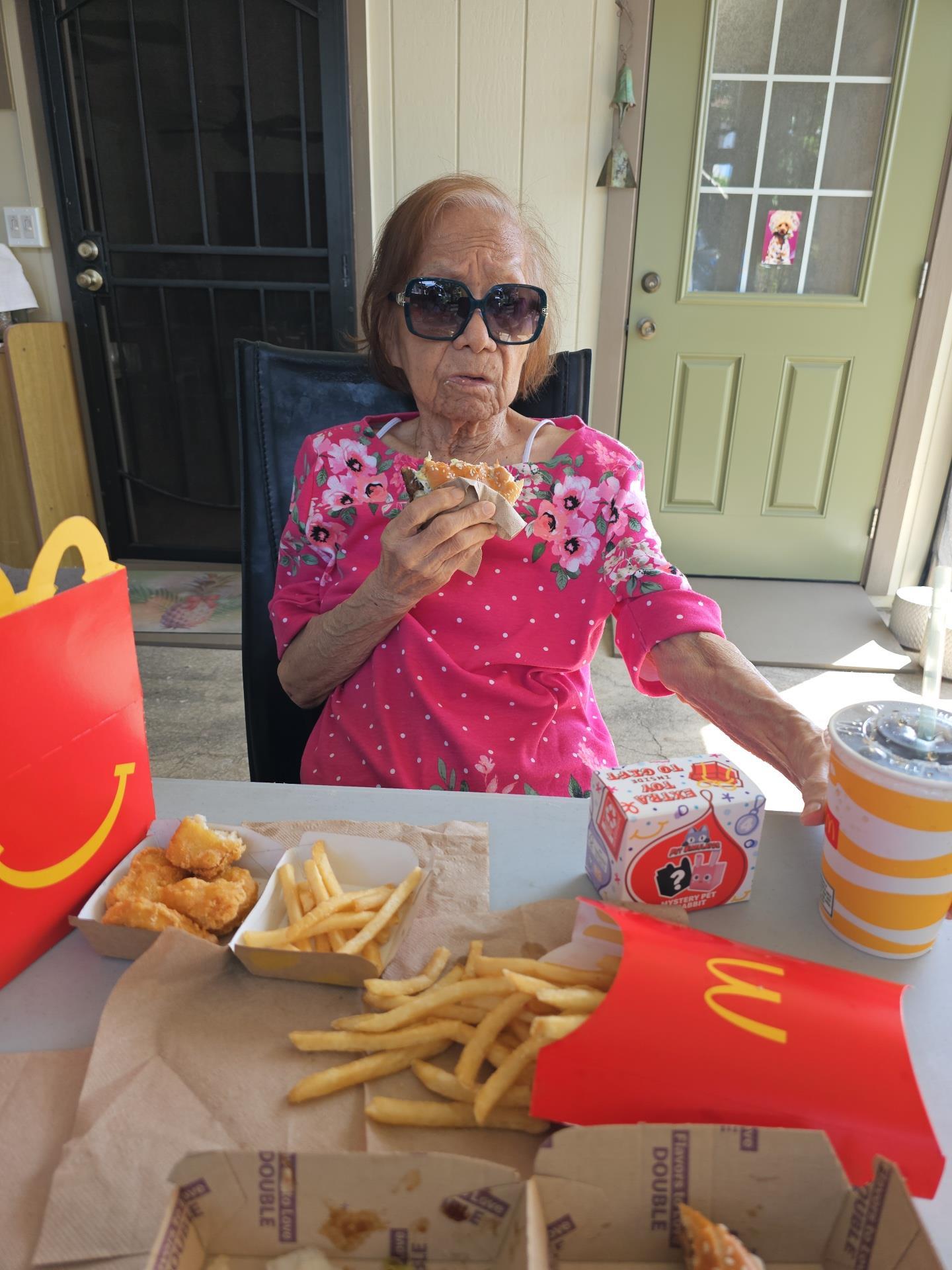 Senior woman in sunglasses relishes fast food in a relaxed outdoor setting.