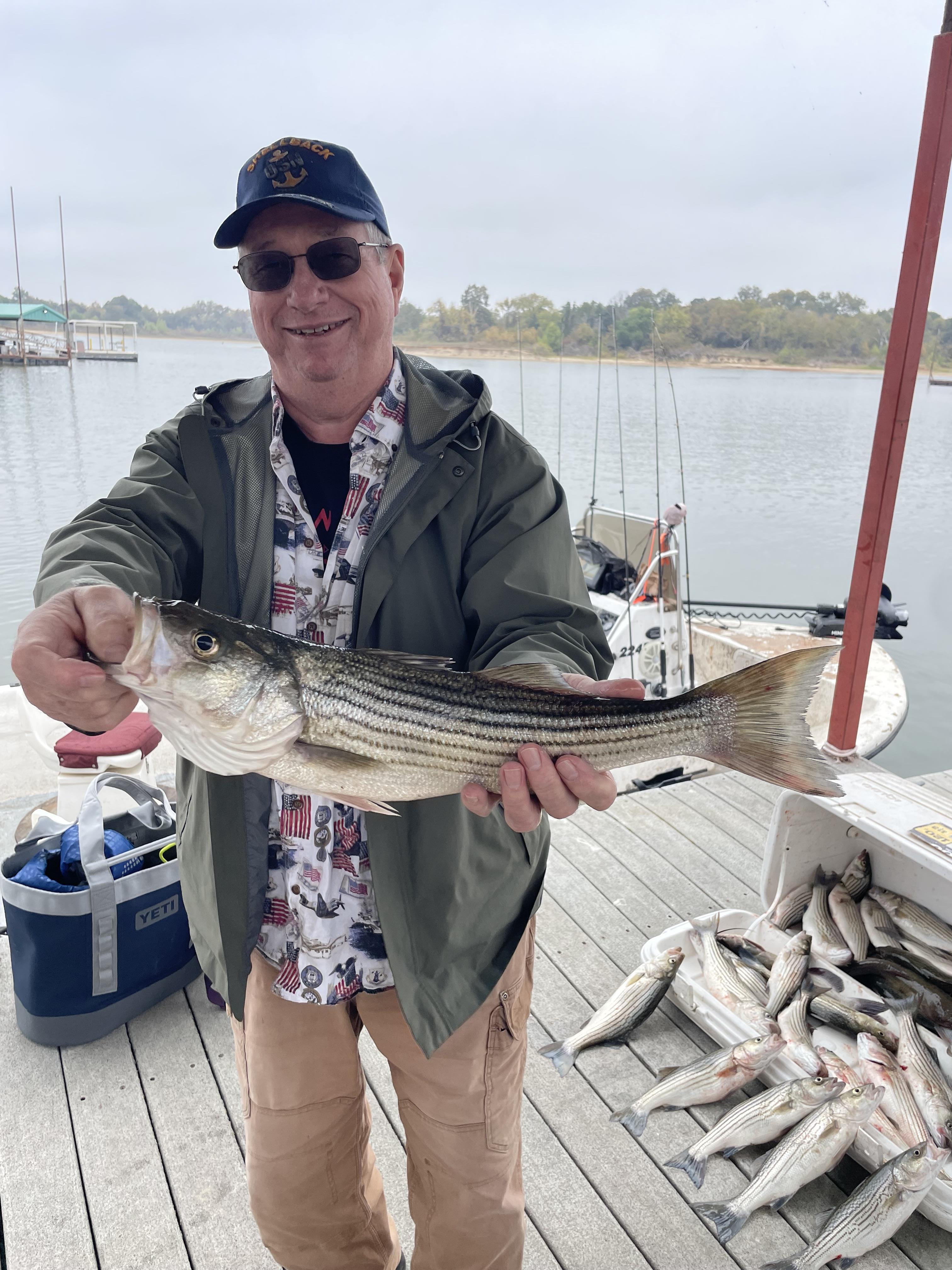 Fisherman proudly holds a large striped bass after a successful fishing trip at the lake.