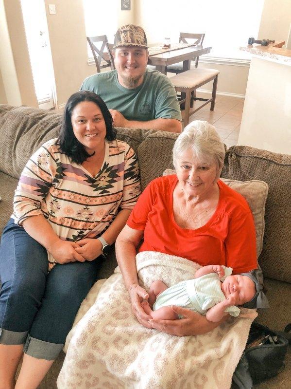 Family members gather together, sharing smiles and moments with a newborn in their home.