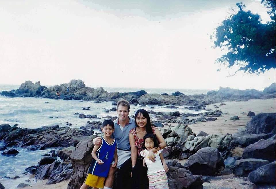A family poses for a picture on a rocky beach while enjoying their time together outdoors.