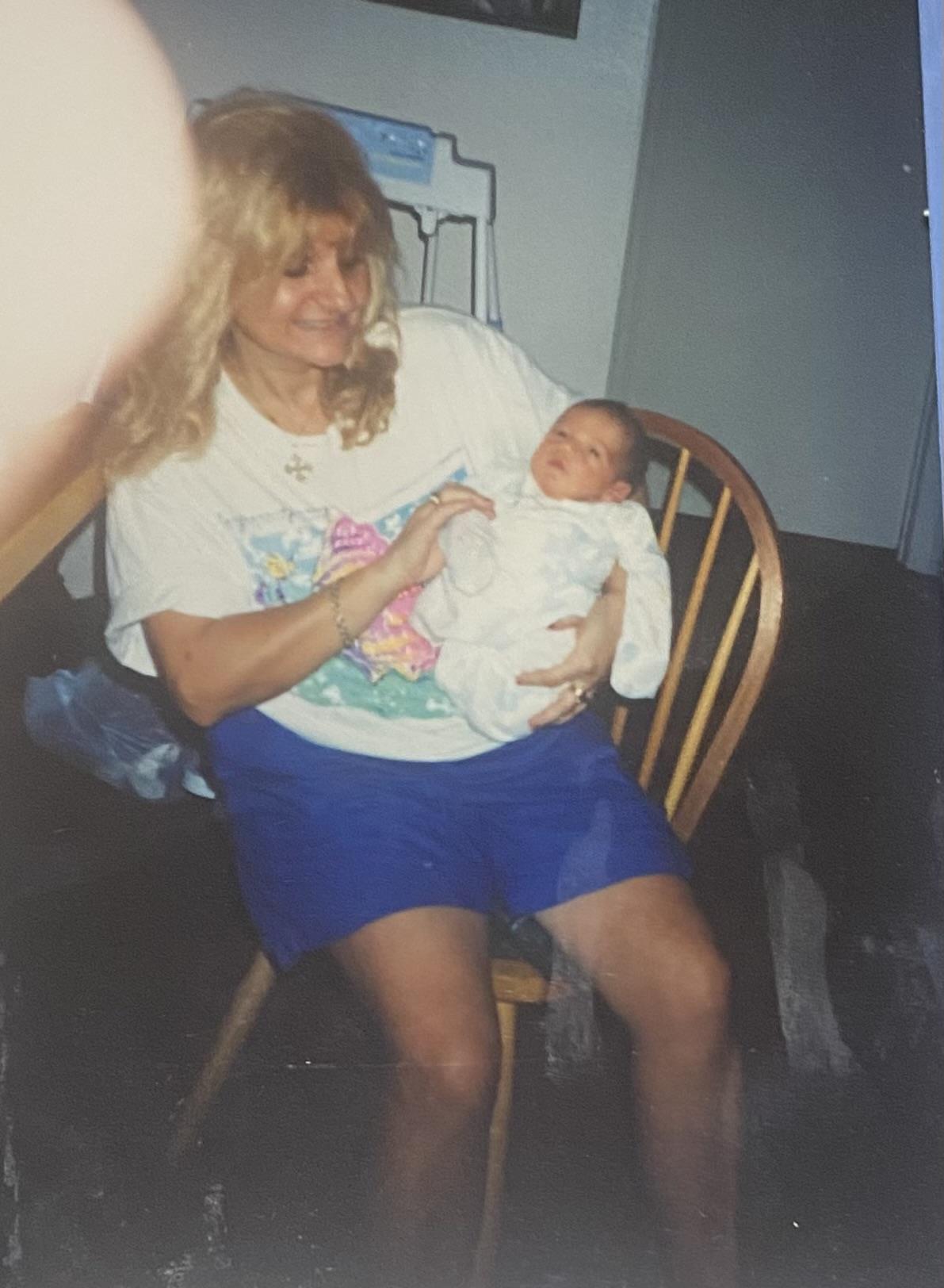 A woman smiles as she holds a newborn baby while sitting in a comfortable chair.