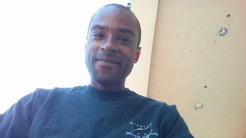 A man enjoys a relaxed moment indoors, smiling as warm light fills the room.