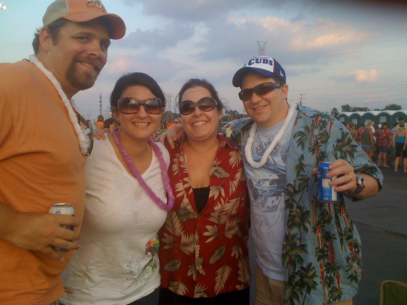 Friends celebrate together at an outdoor festival, dressed casually and smiling happily at sunset.