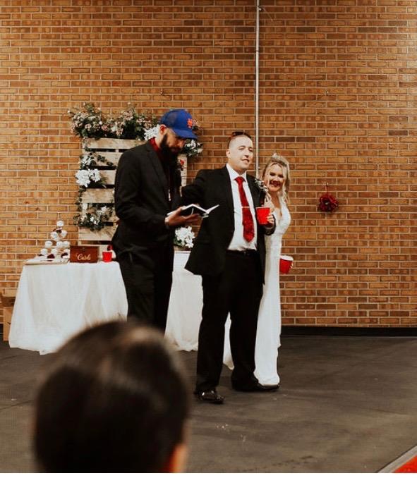 Guests gather around two speakers during a festive event in a rustic, brick-walled venue.