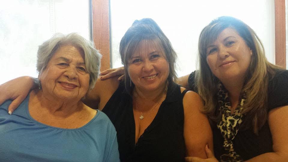 Three women smile happily while sitting close together, sharing a joyful moment at a family event.