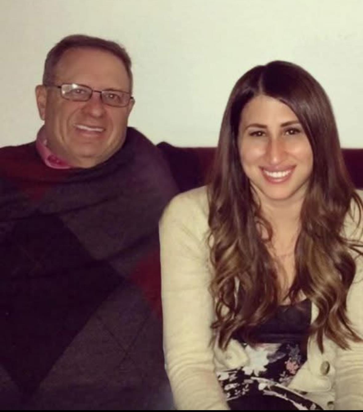 A man and woman share warm smiles, sitting closely together on a couch.
