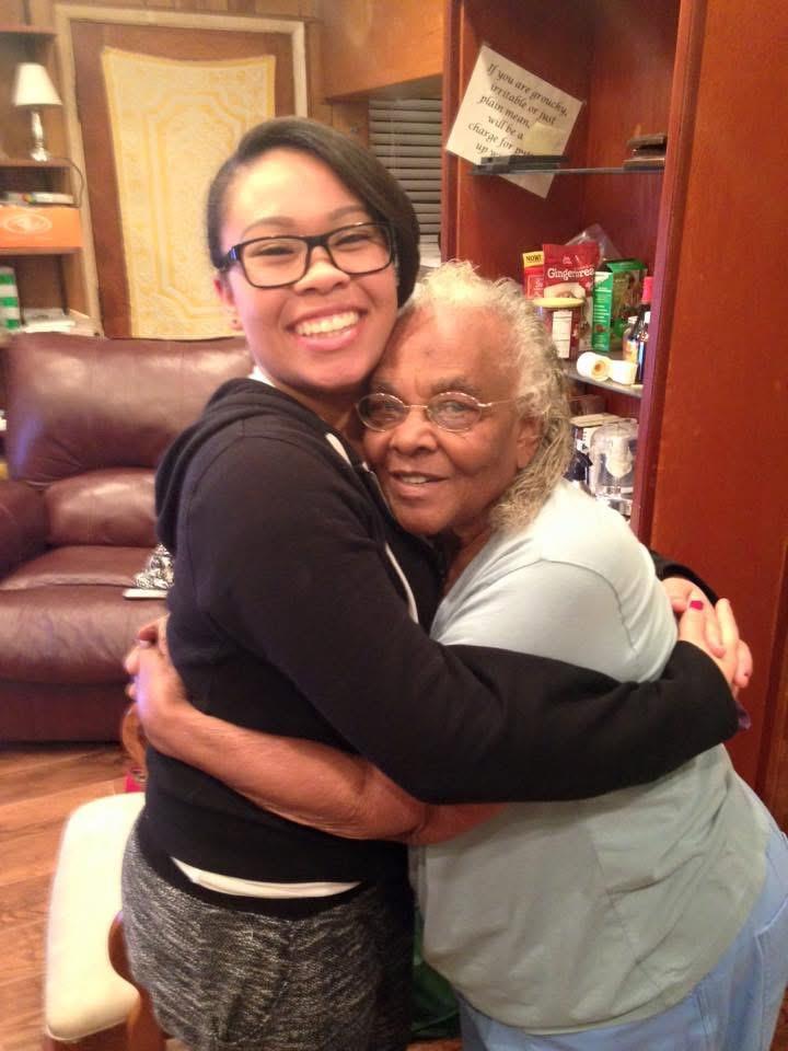 A young woman joyfully hugs an elderly woman in a warm, inviting living room setting.