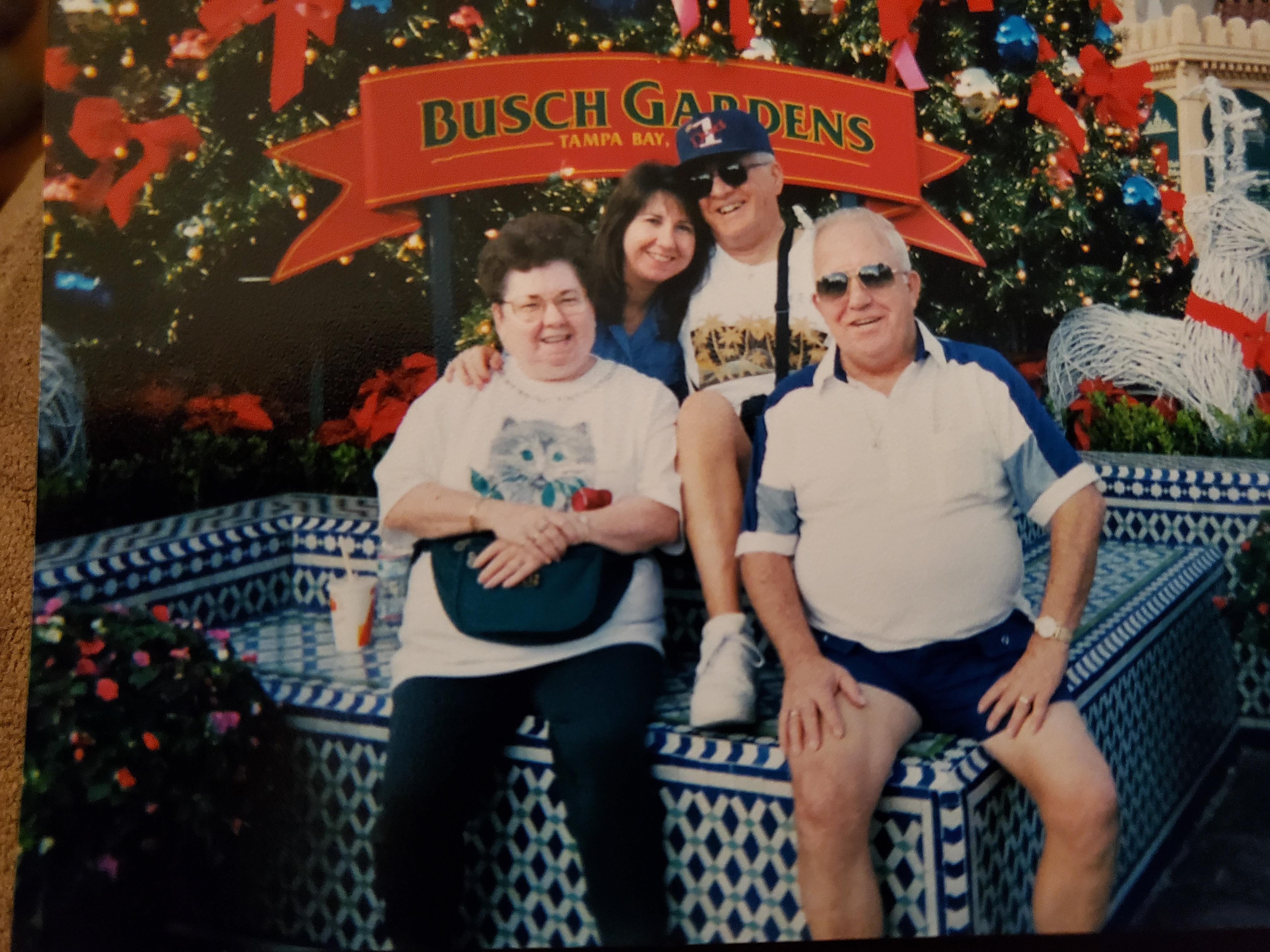Four family members gather on a bench at a festive theme park, surrounded by decorations.
