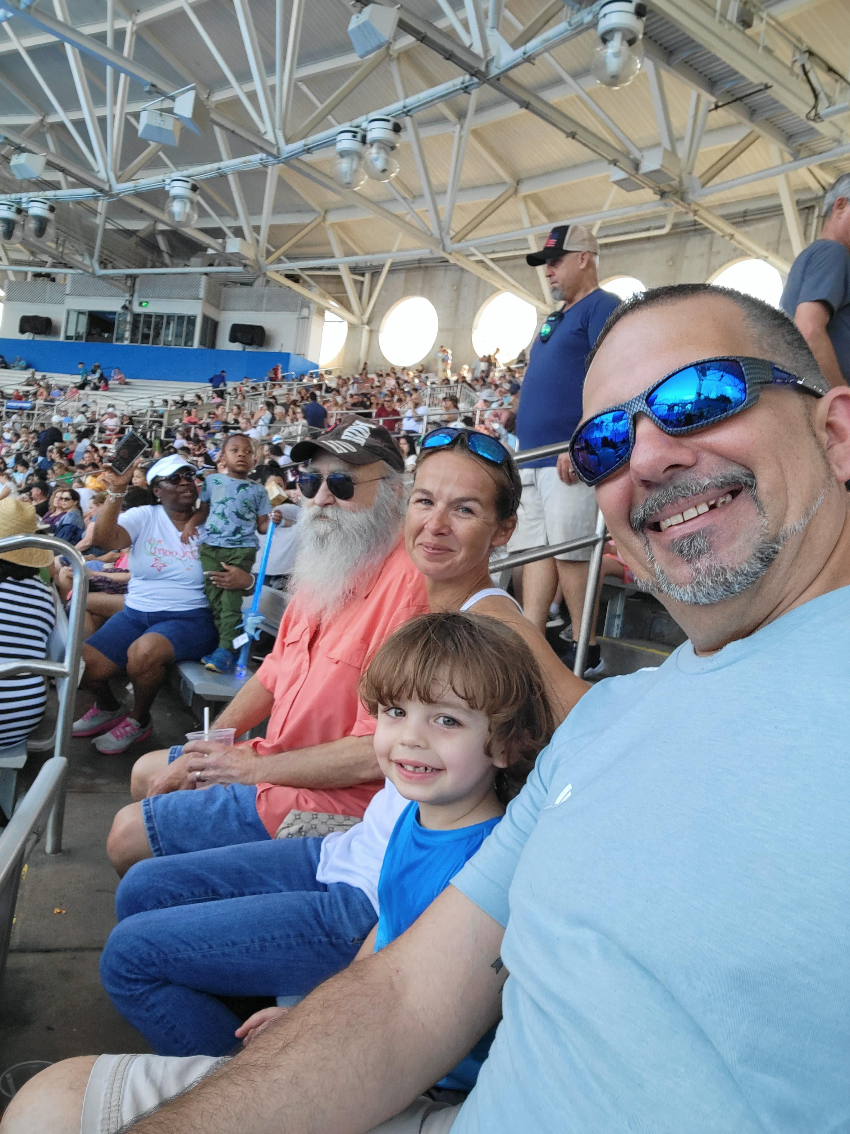 Family smiles together while seated in the stands at a sports event with a large audience.