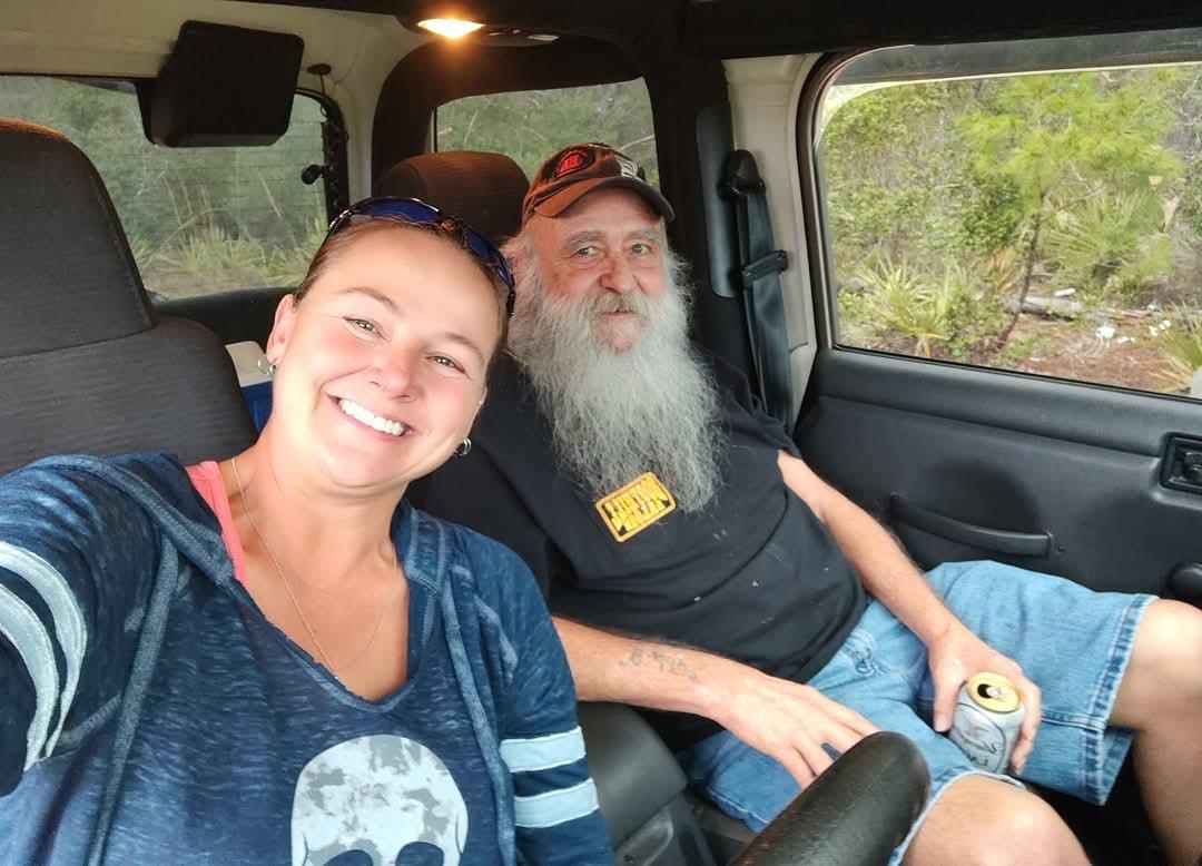 A smiling couple shares a joyful moment inside a vehicle surrounded by greenery on a sunny day.