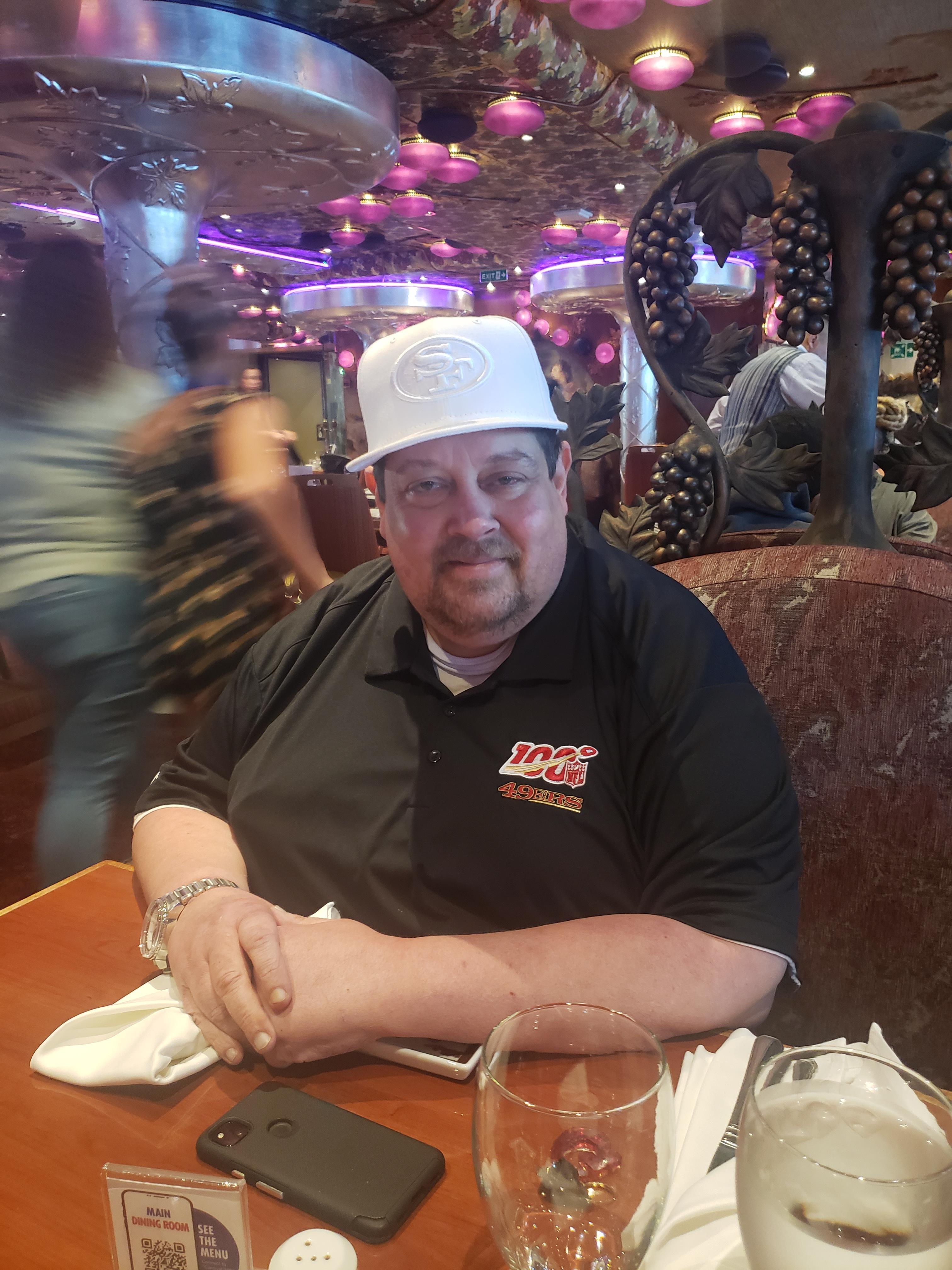 A man seated at a table in a vibrant restaurant filled with colorful decor and busy patrons.