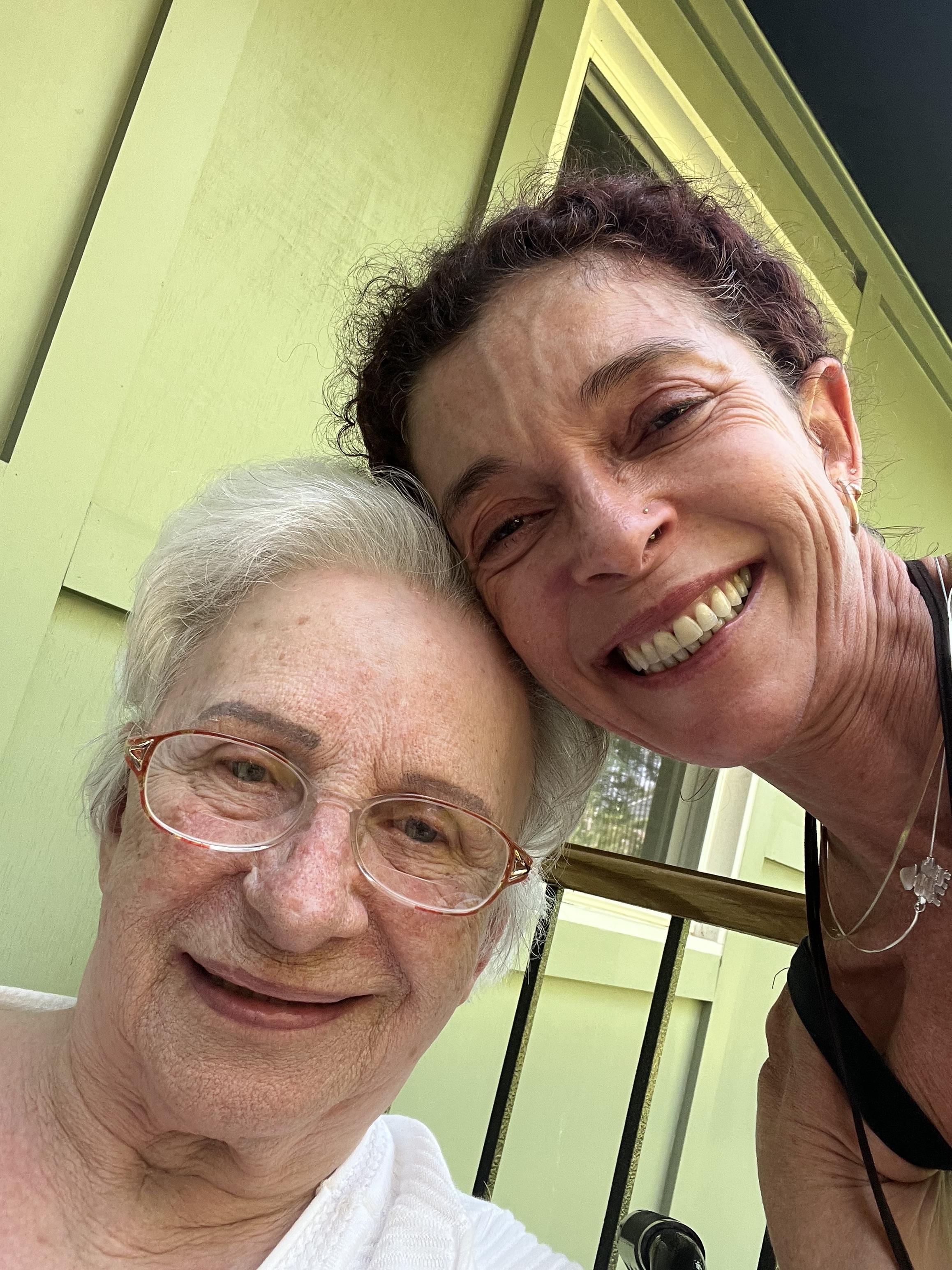 Grandmother and granddaughter share smiles and laughter outdoors in bright sunlight.
