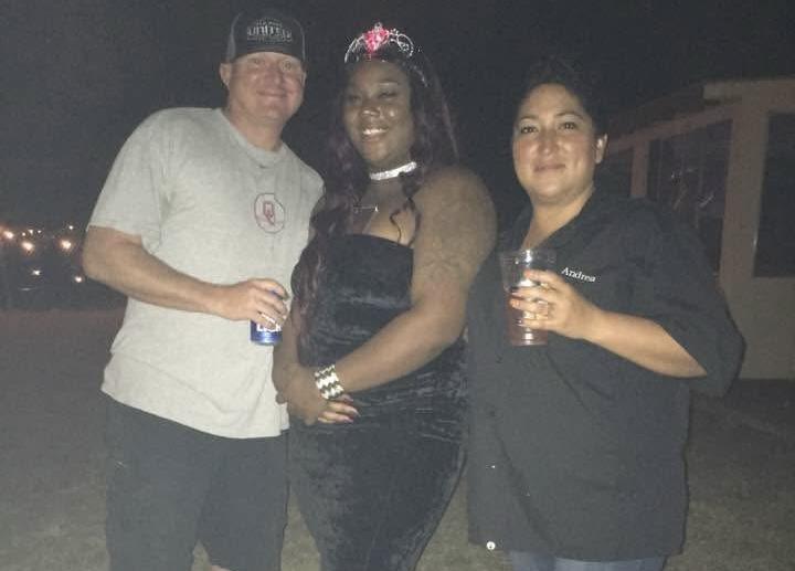 Group of three friends enjoy drinks and laughter during a lively evening event outdoors.