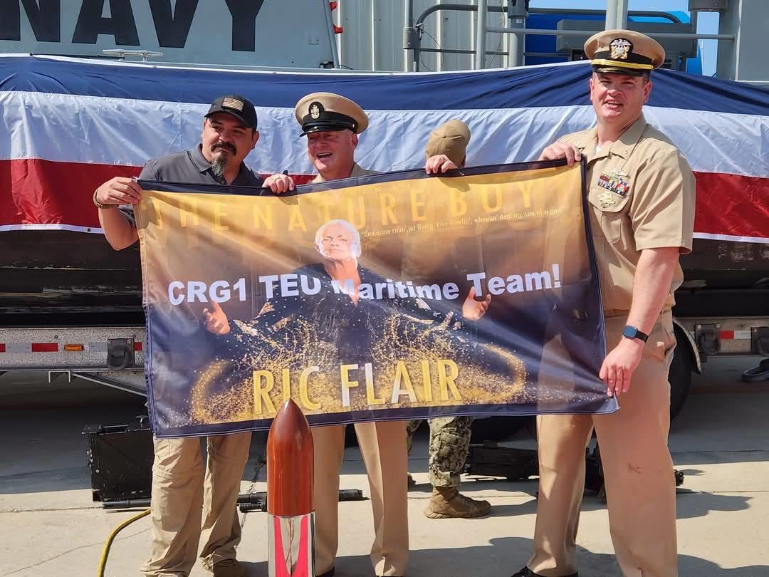 Military members proudly display a banner at a celebration event aboard a naval vessel.