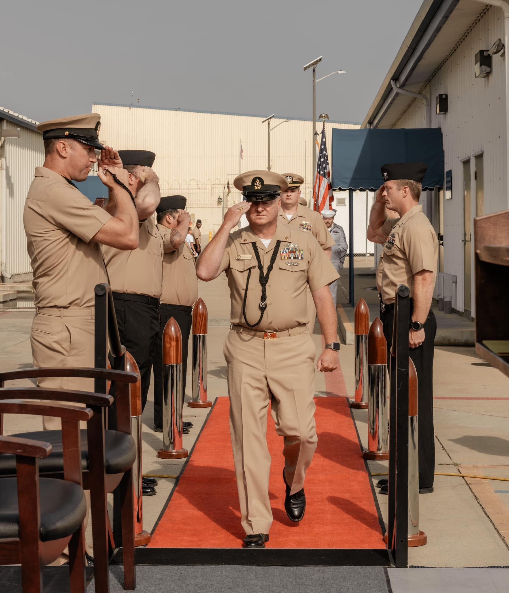 Uniformed service members participate in a formal salute during a ceremony at a naval base.