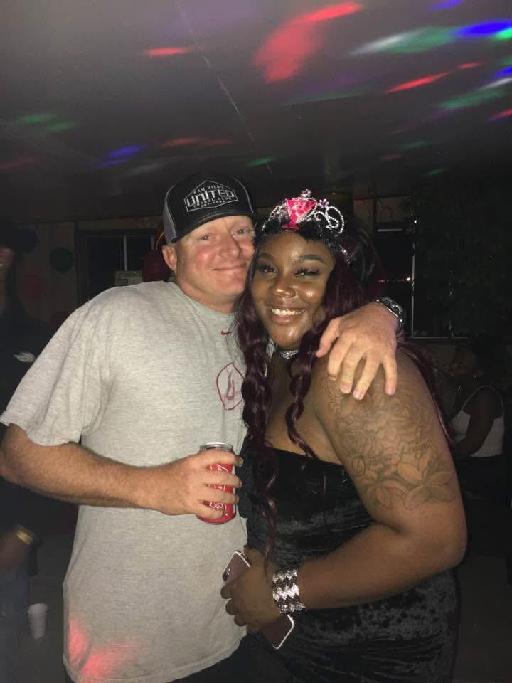 A joyful couple embraces at a lively celebration filled with colorful lights and music.