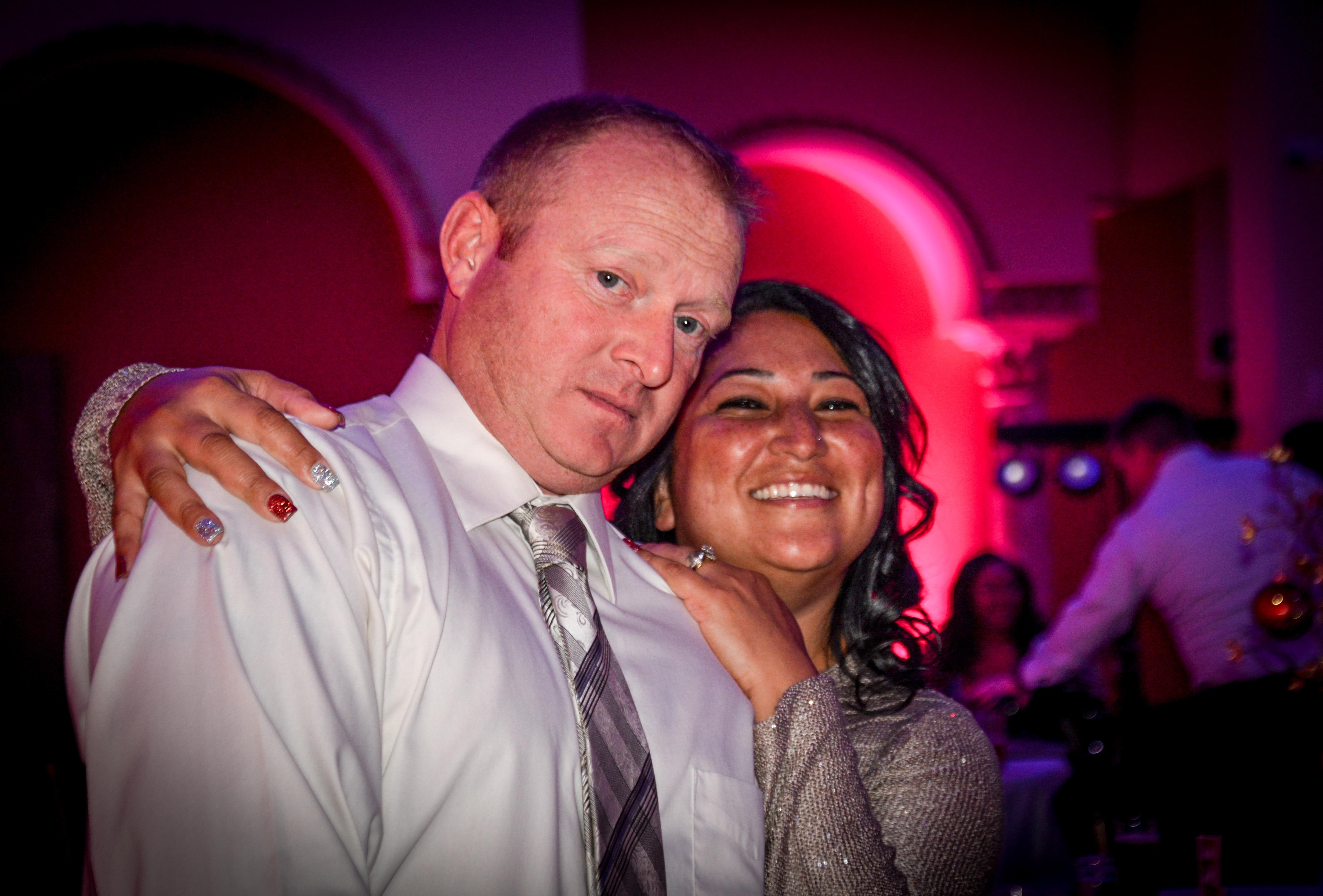 A joyful couple enjoys their time at a bustling indoor party filled with vibrant lights.