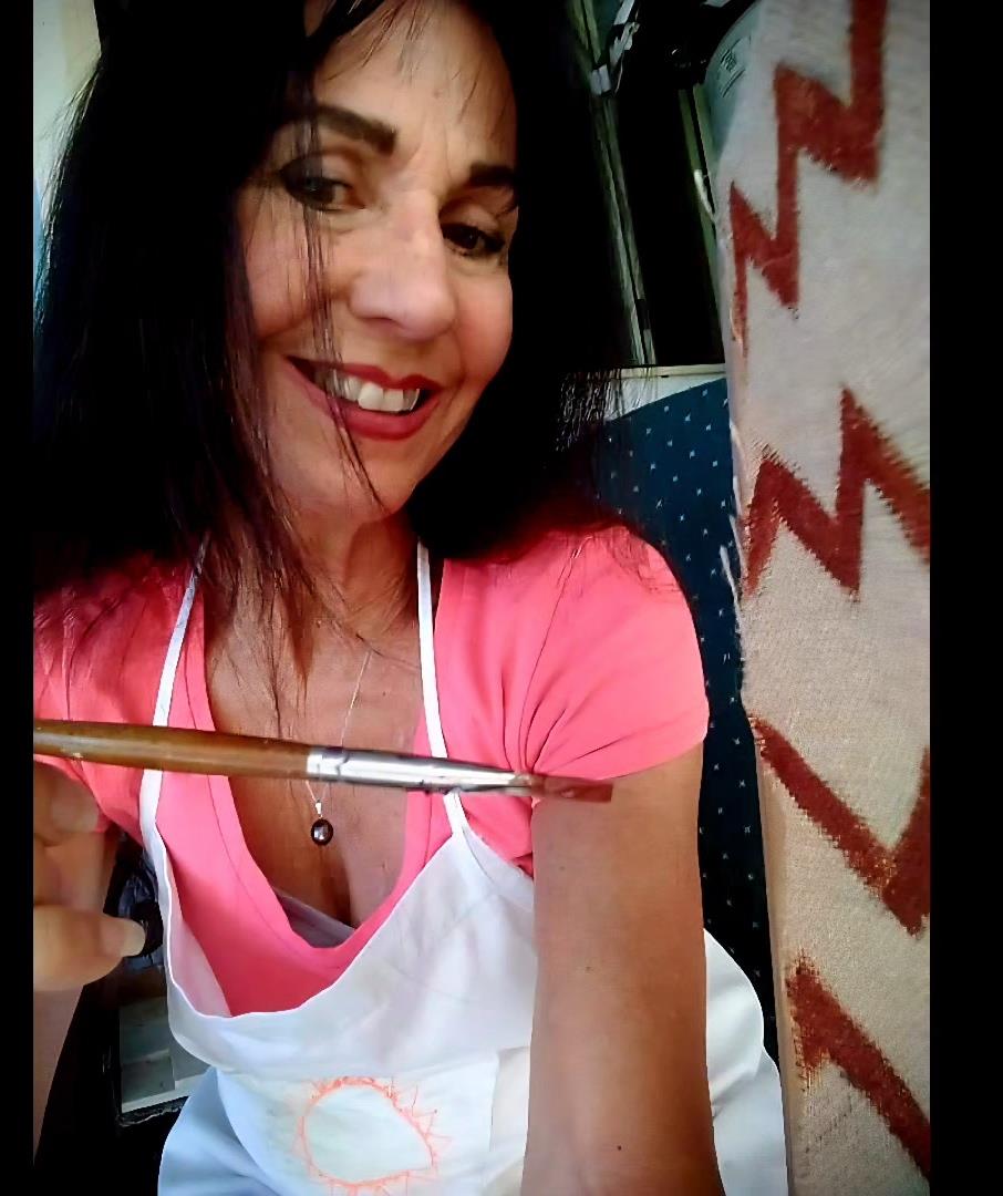 Woman smiles while holding a paintbrush next to colorful designs on a wall in the background.