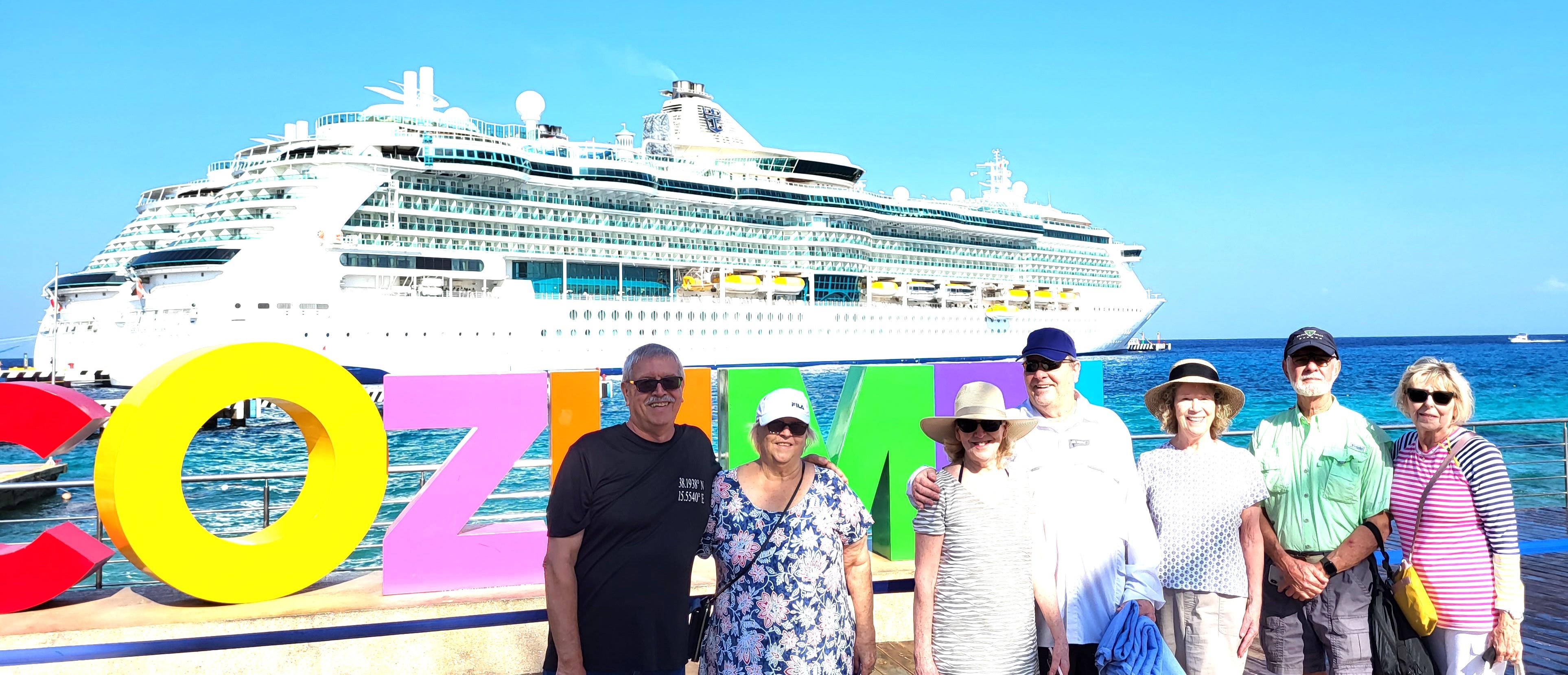 Groups of tourists enjoy a sunny day at Cozumel port with a cruise ship docked behind them.