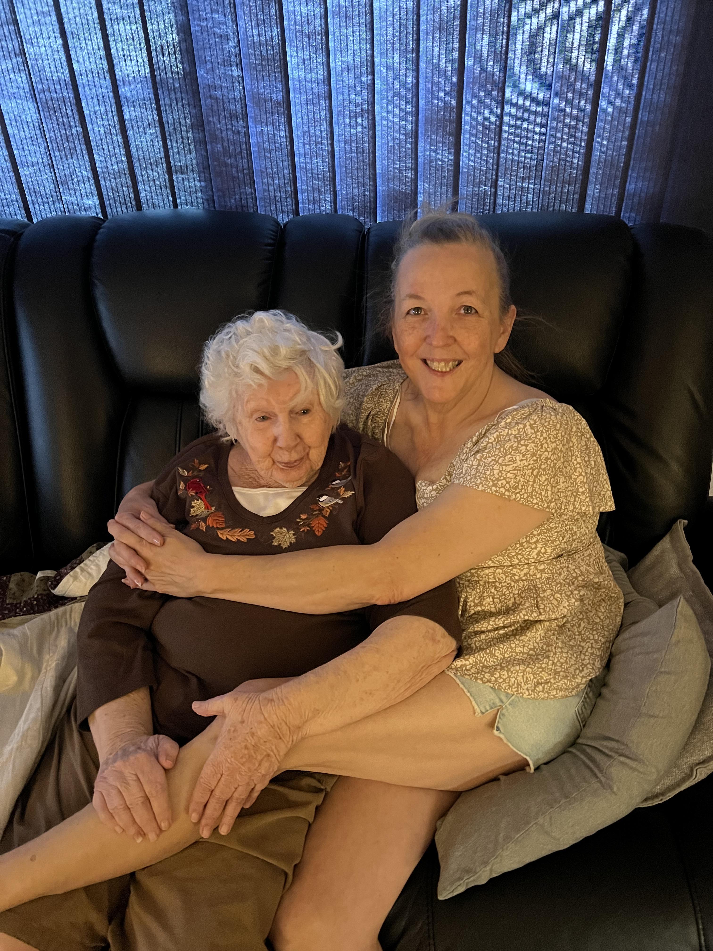 Two women enjoy a heartwarming moment together, smiling while seated on a couch.