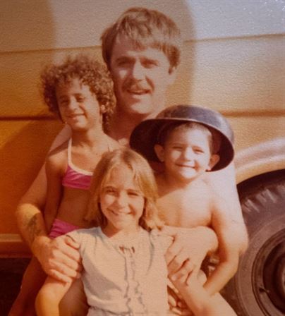 A man holding children in front of a car