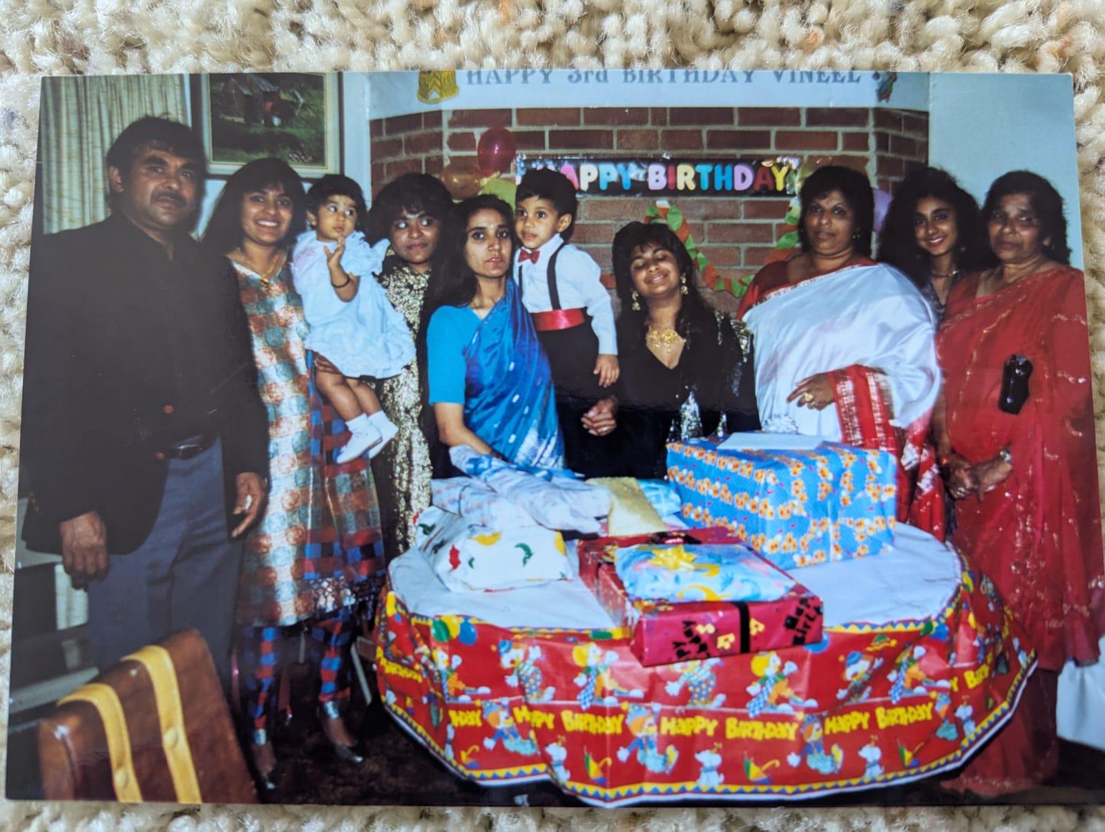 Group joyfully celebrates with cake and gifts, filled with smiles and laughter.