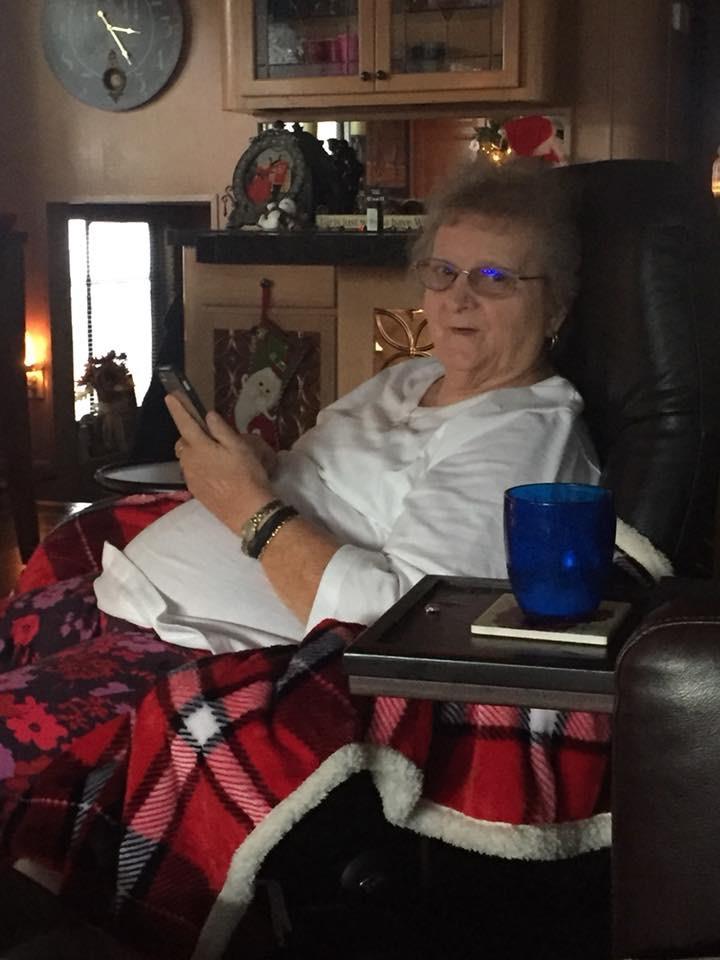 Woman sits comfortably in a chair, wrapped in a blanket, checking her phone at home.