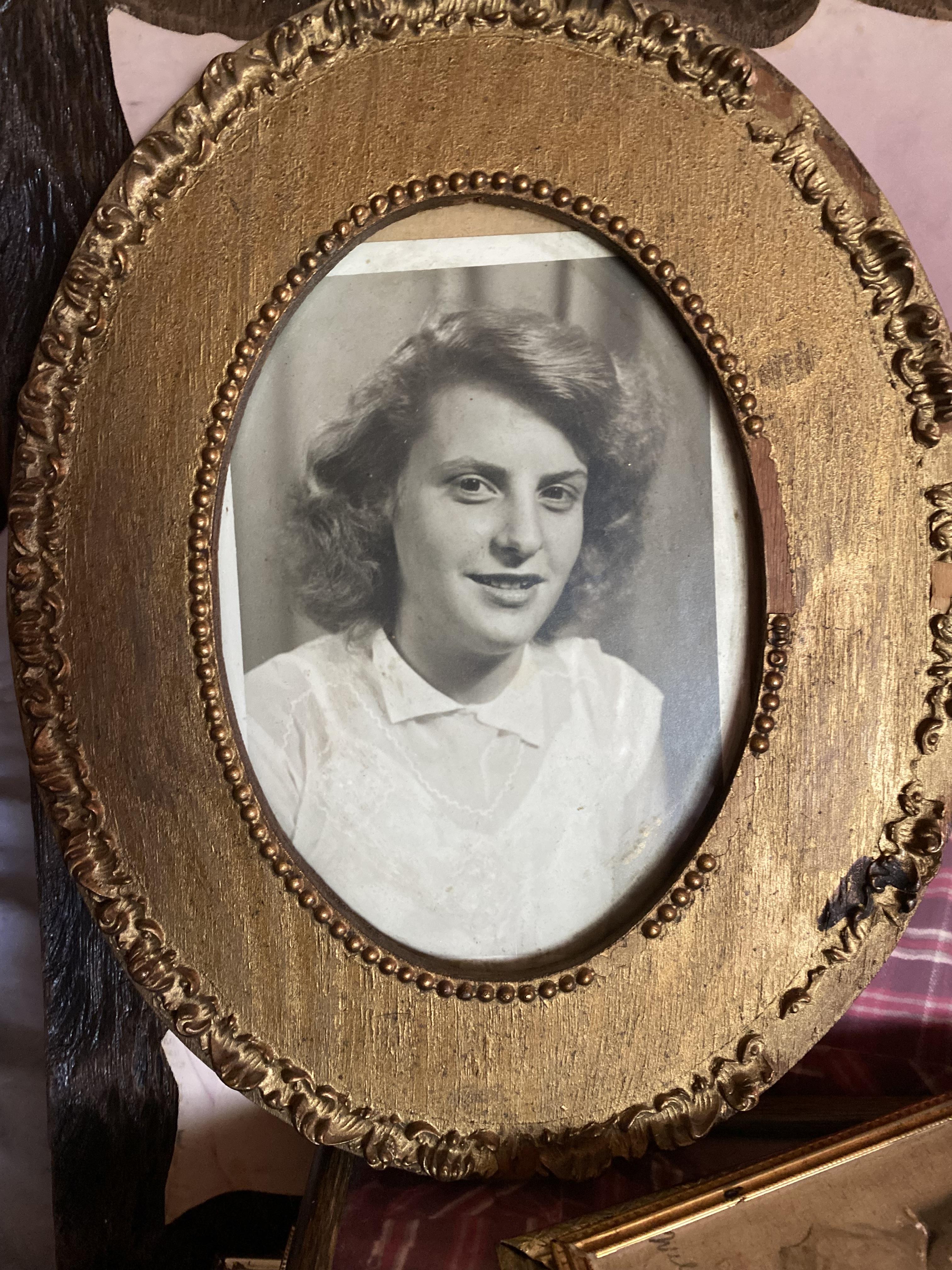 A young woman with curly hair smiles from a vintage oval frame in an old-fashioned setting.