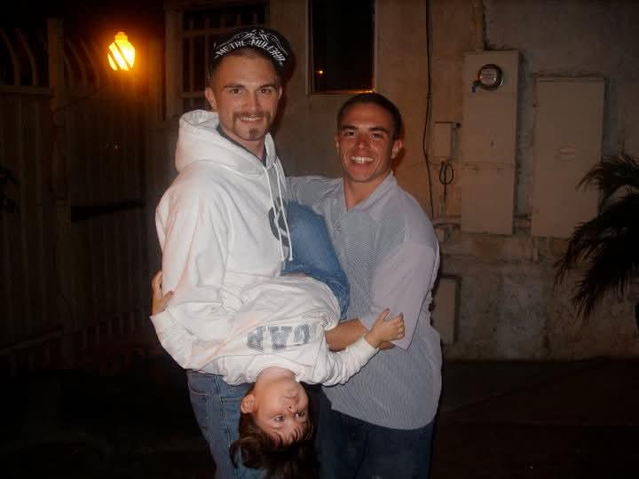 Friends share laughter while one playfully lifts another upside down under warm street lights.