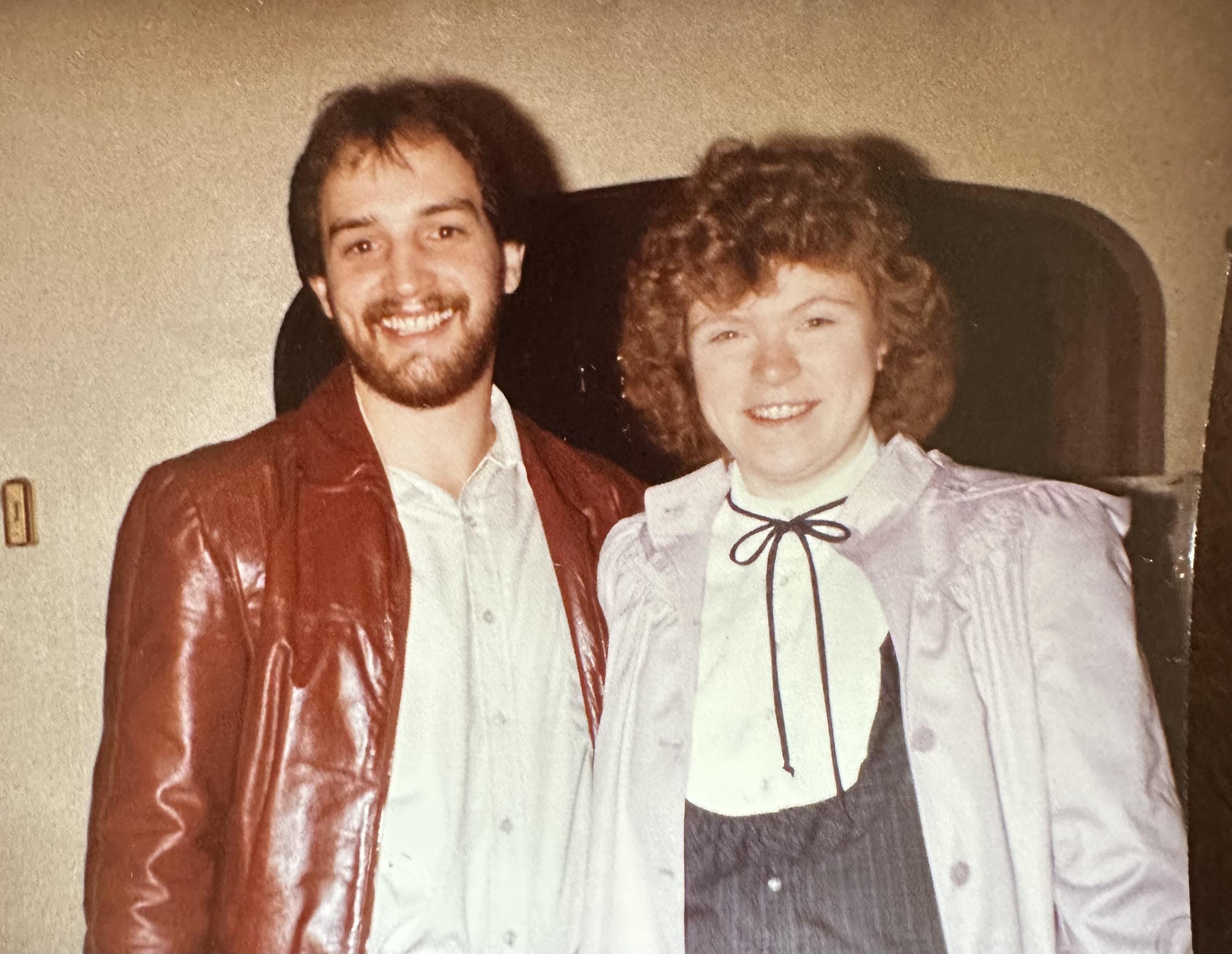 A man and a woman are posing happily together at a social event in the 1980s.