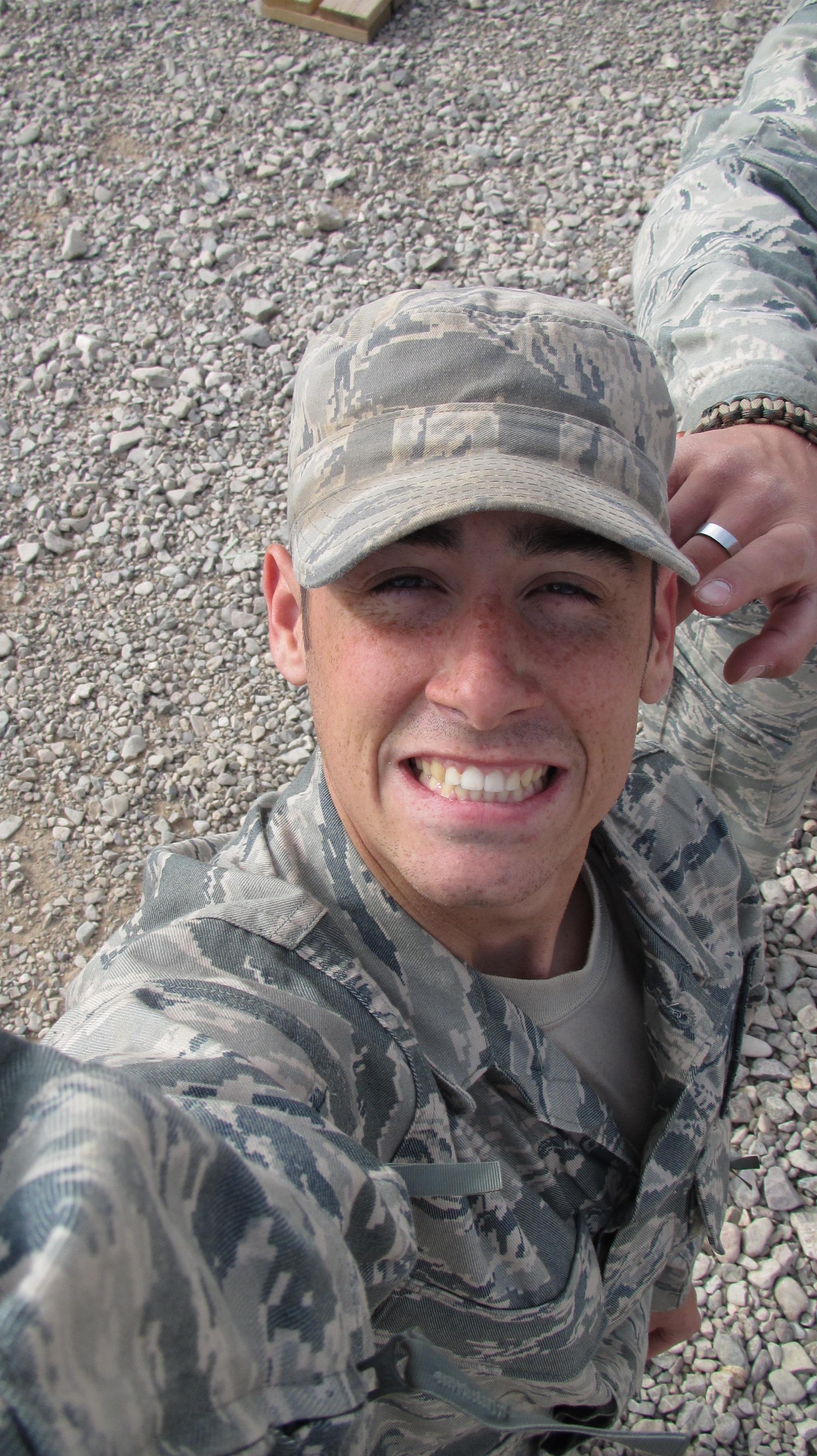 A cheerful service member smiles while taking a selfie in a rocky outdoor location during training.