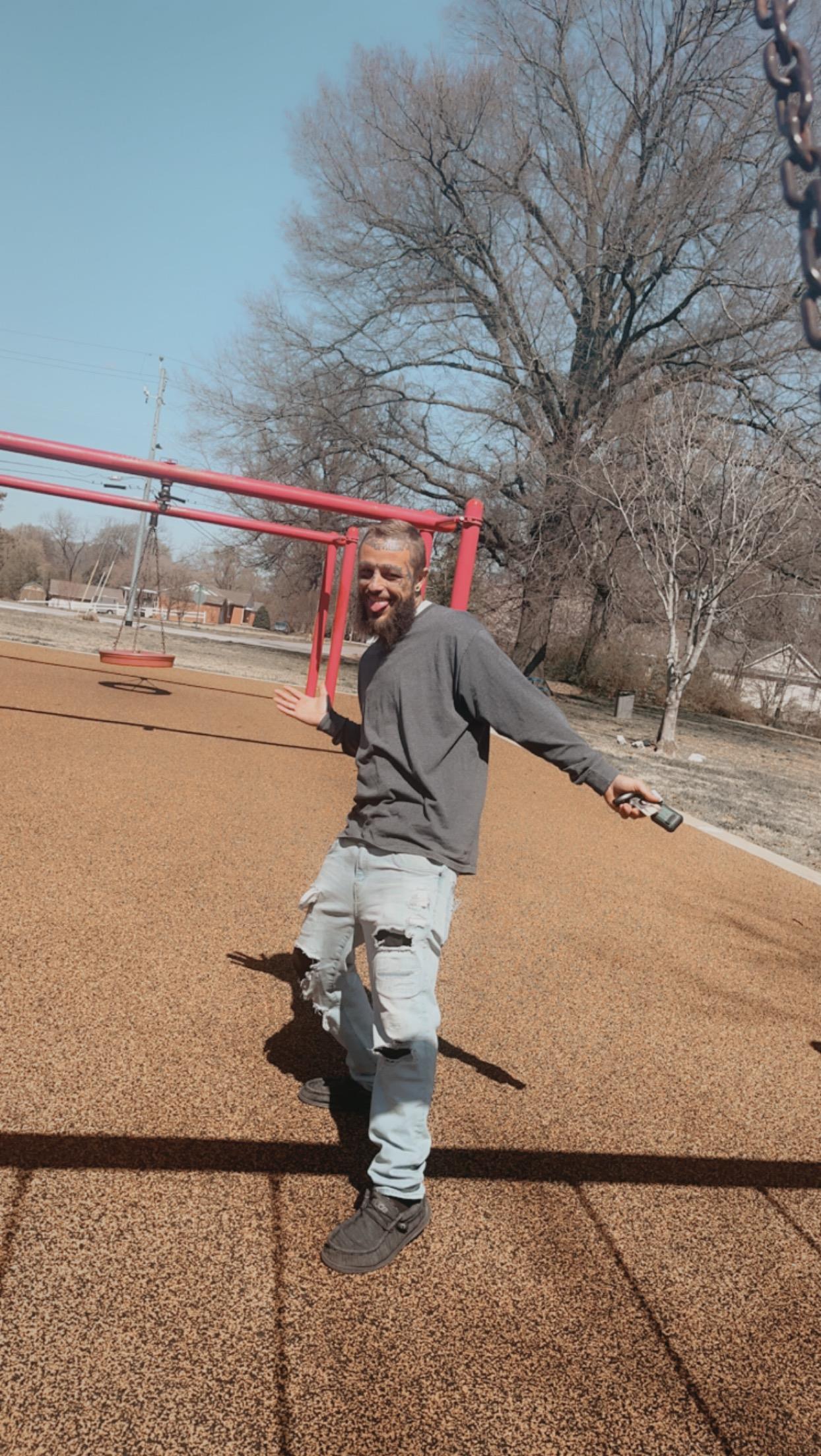 A man swings joyfully in a park, surrounded by trees under clear blue skies during winter.