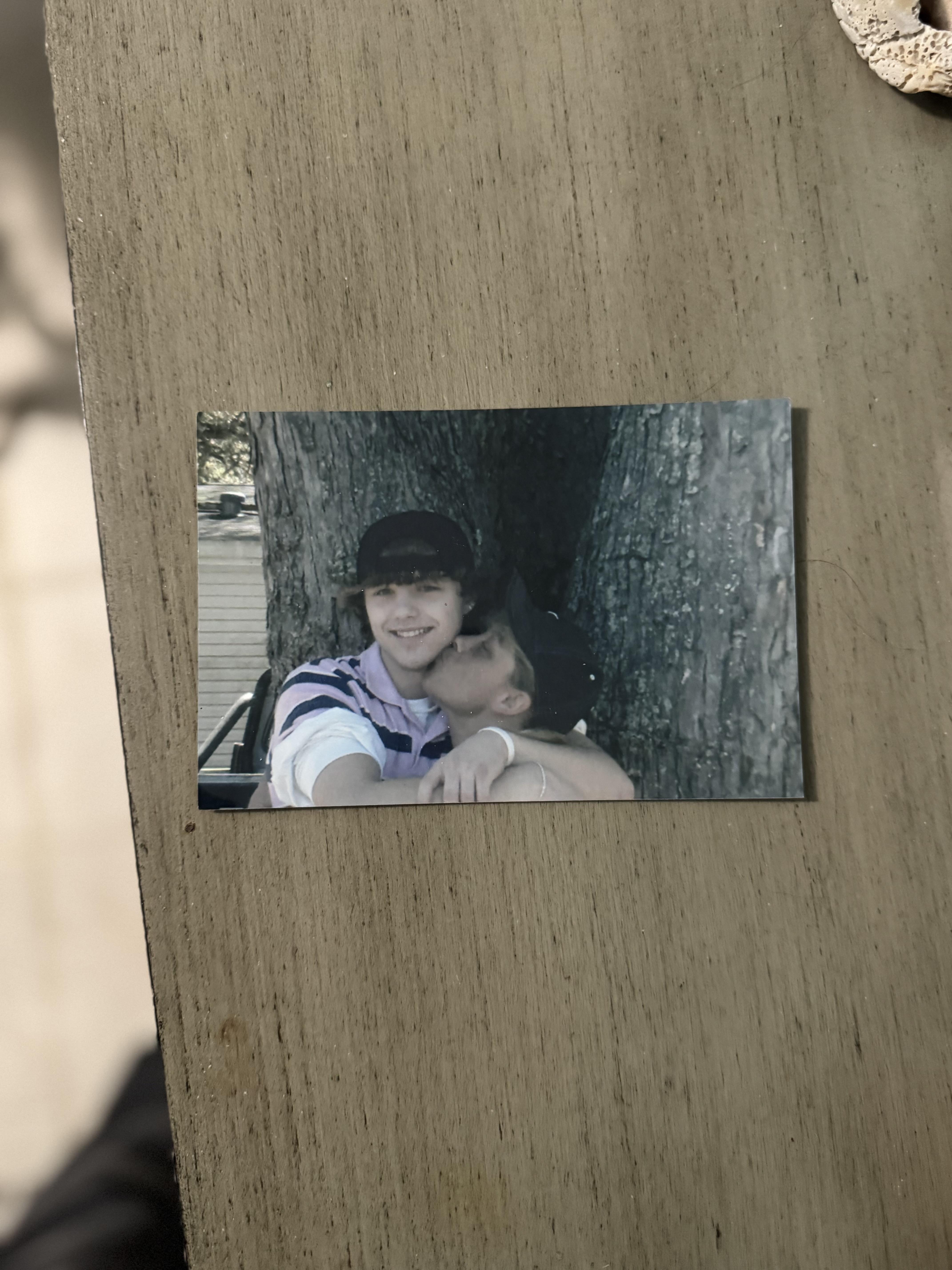A parent holds a baby close, enjoying a quiet moment outdoors by a large tree.