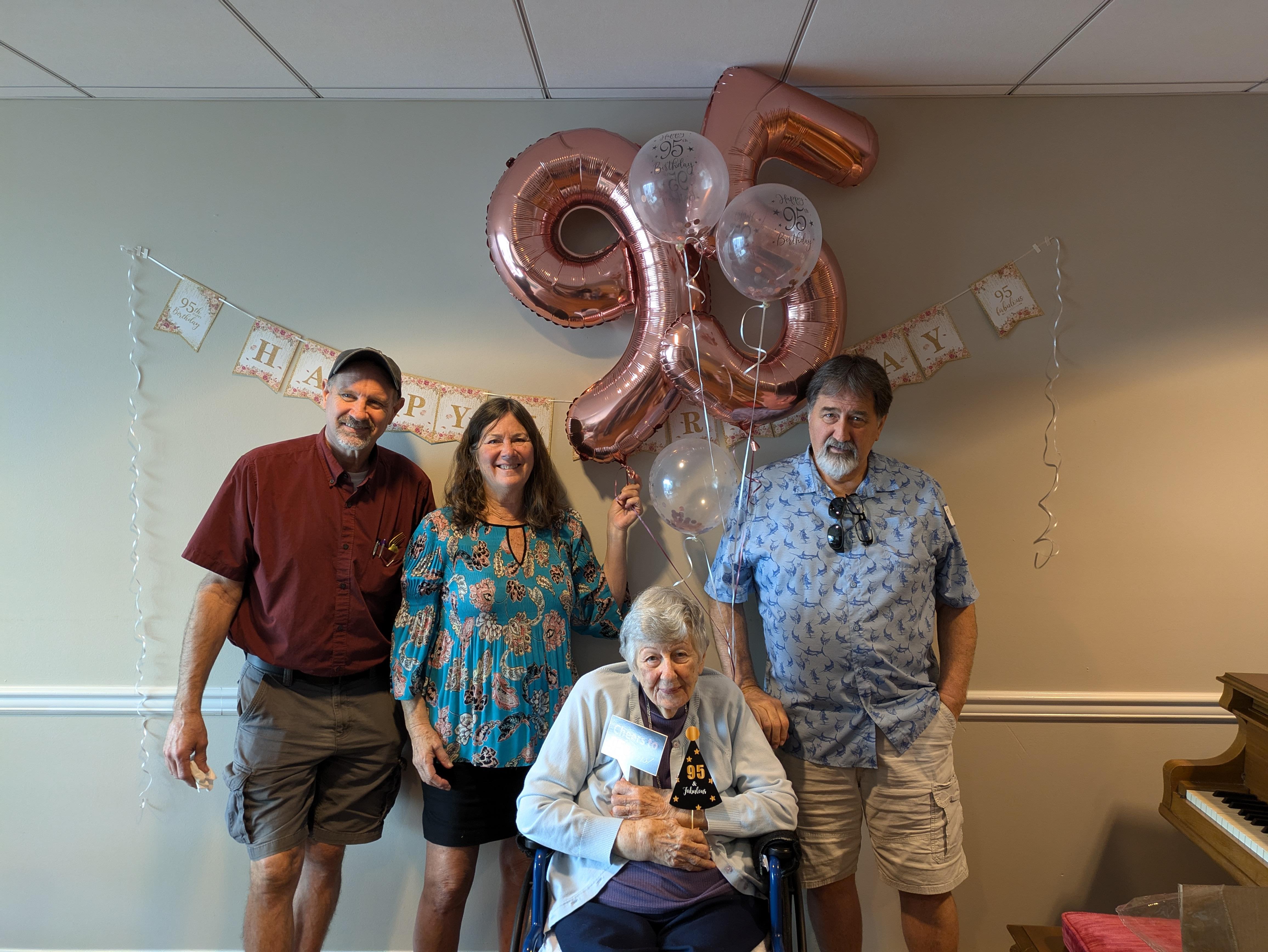 Family gathers to celebrate a joyful elder's 95th birthday with balloons and smiles.