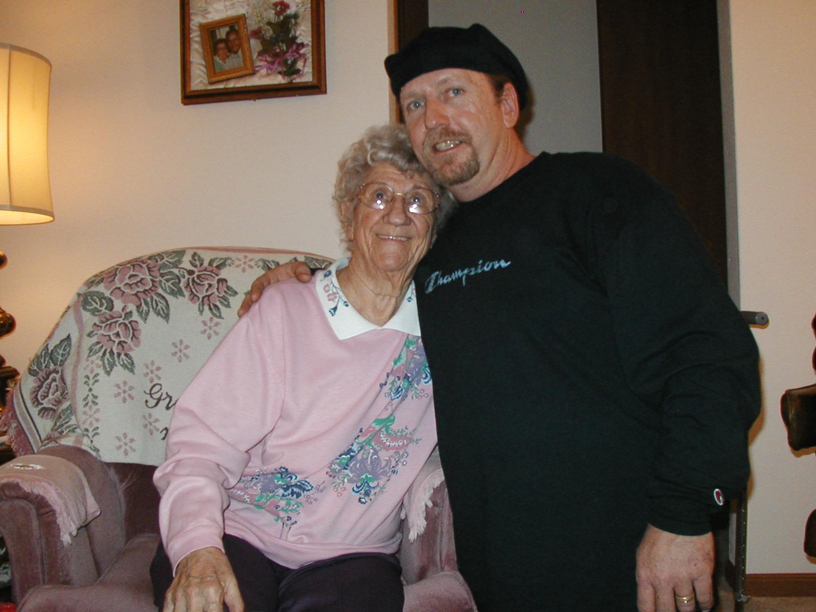 Elderly woman wearing glasses enjoys time with a companion in a warm living room setting.