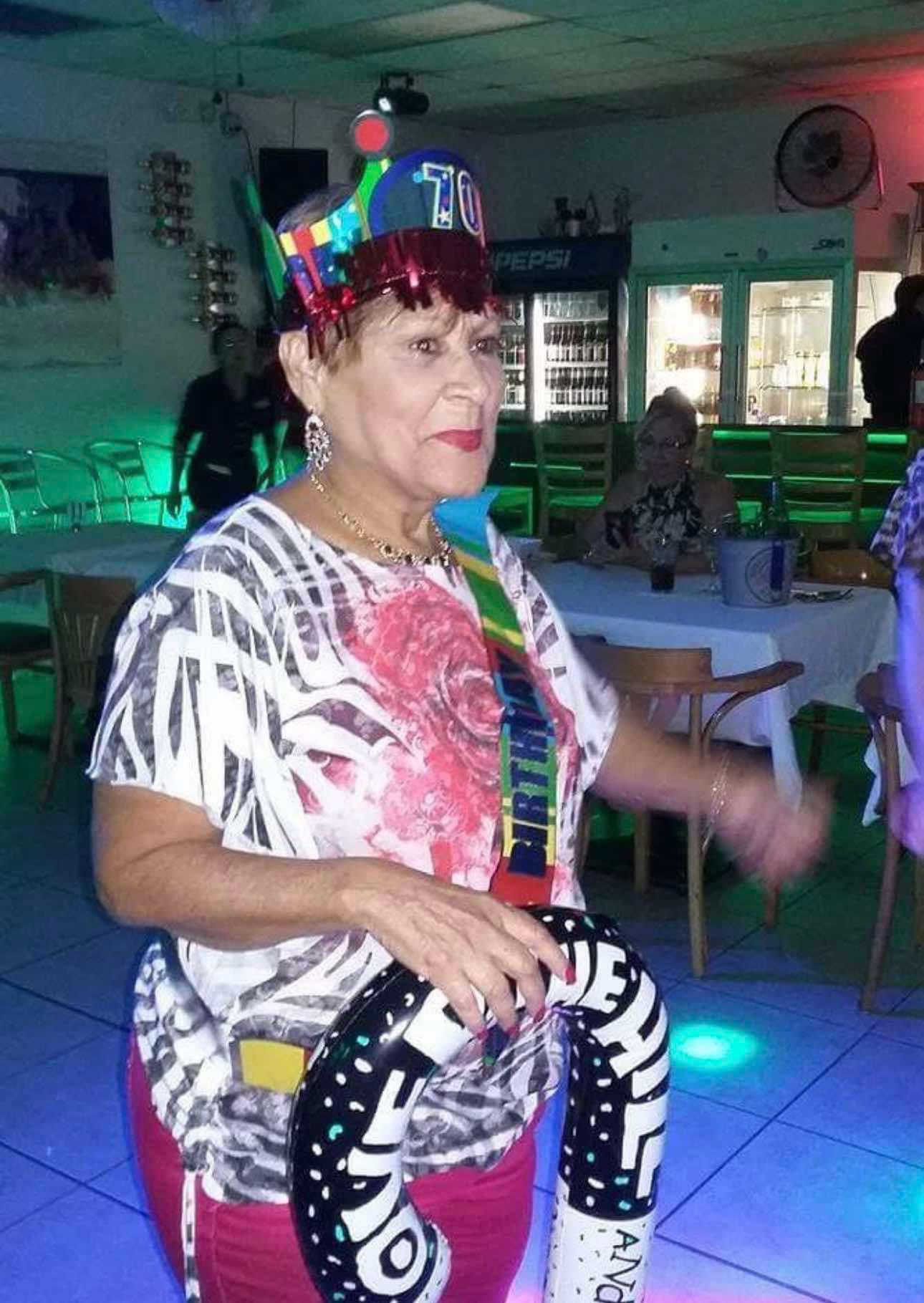 An elderly woman wearing a festive crown dances joyfully at a vibrant party surrounded by friends.