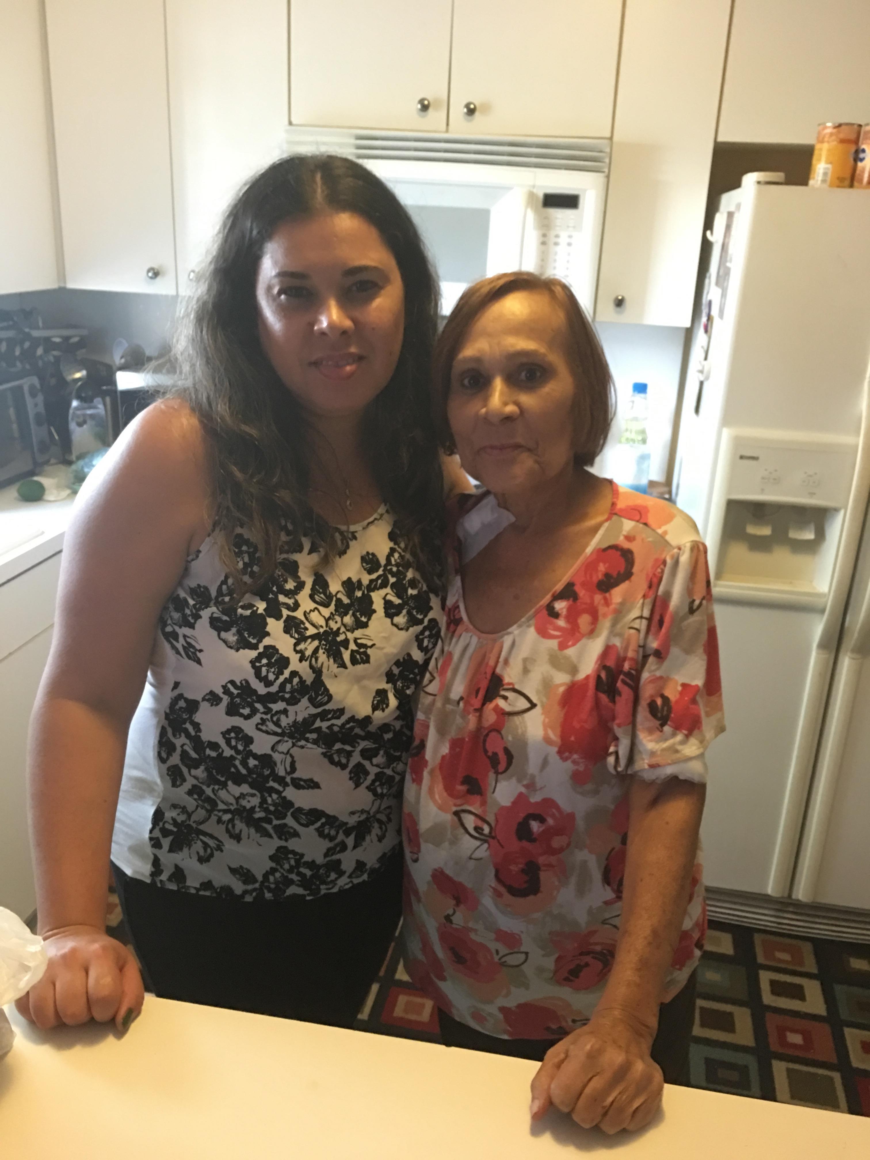 Two women share a moment in a bright kitchen, smiling and enjoying each other's company.