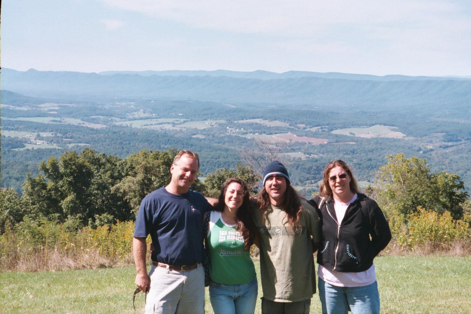 Friends stand together smiling with a beautiful mountain landscape behind them on a sunny day.
