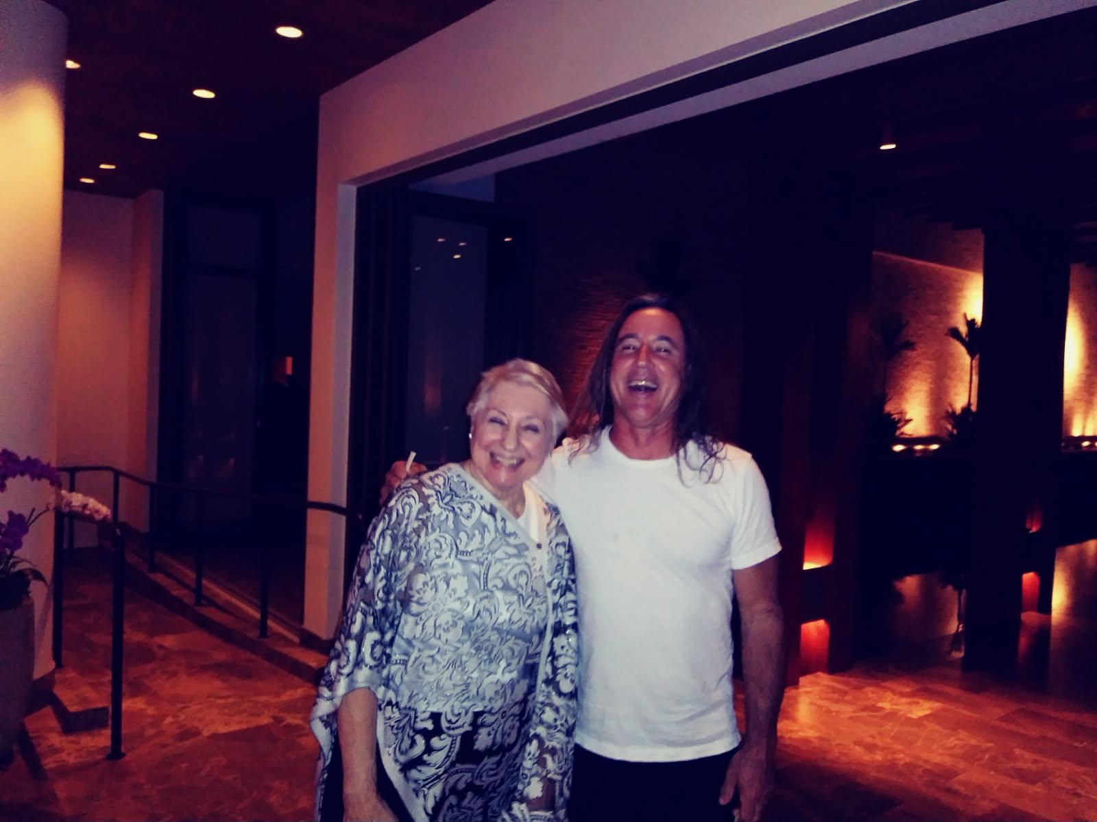 A cheerful couple stands together, smiling brightly in a softly lit indoor environment at night.