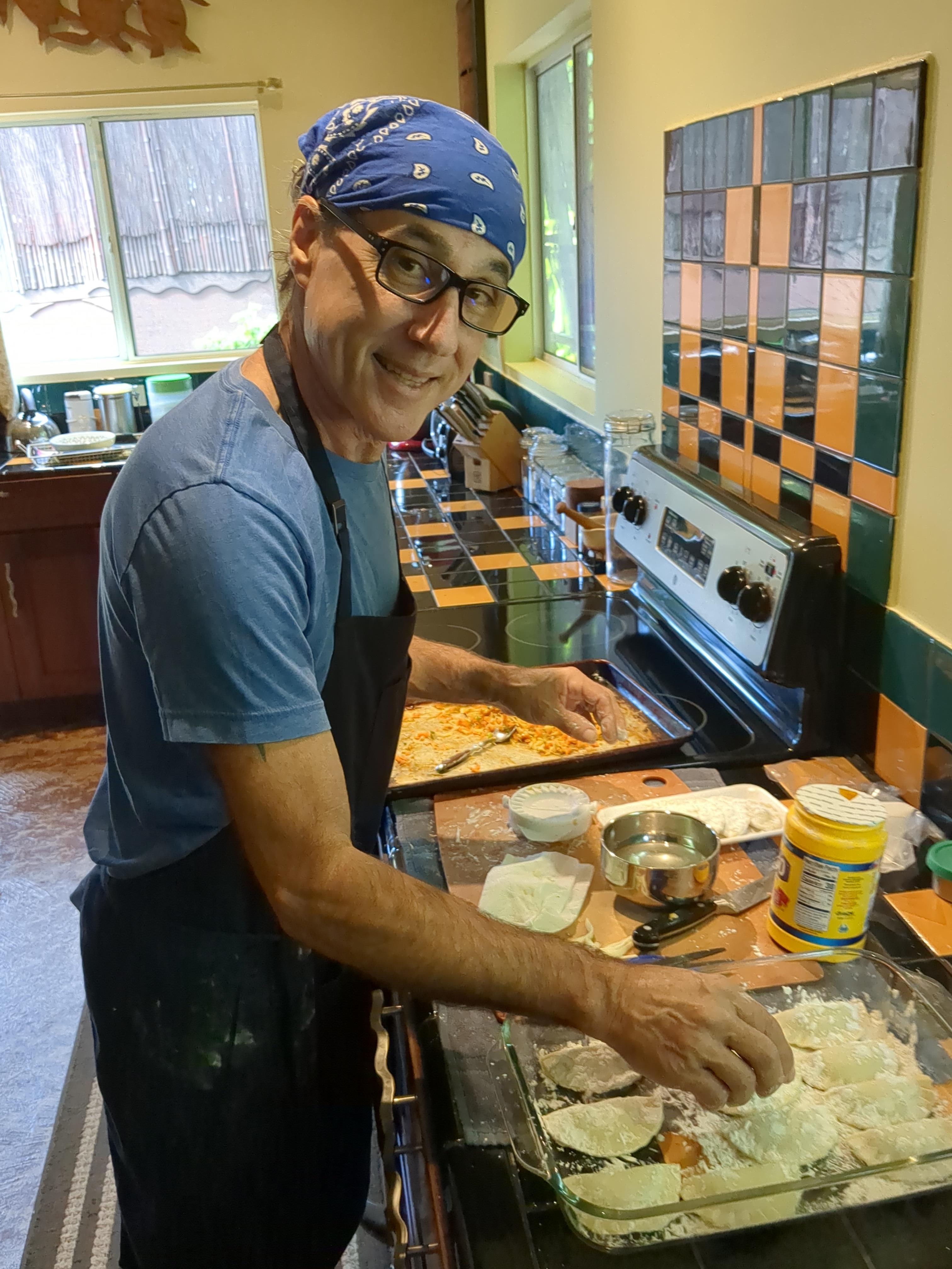 A man is focused on cooking, adding ingredients in a vibrant kitchen filled with natural light.