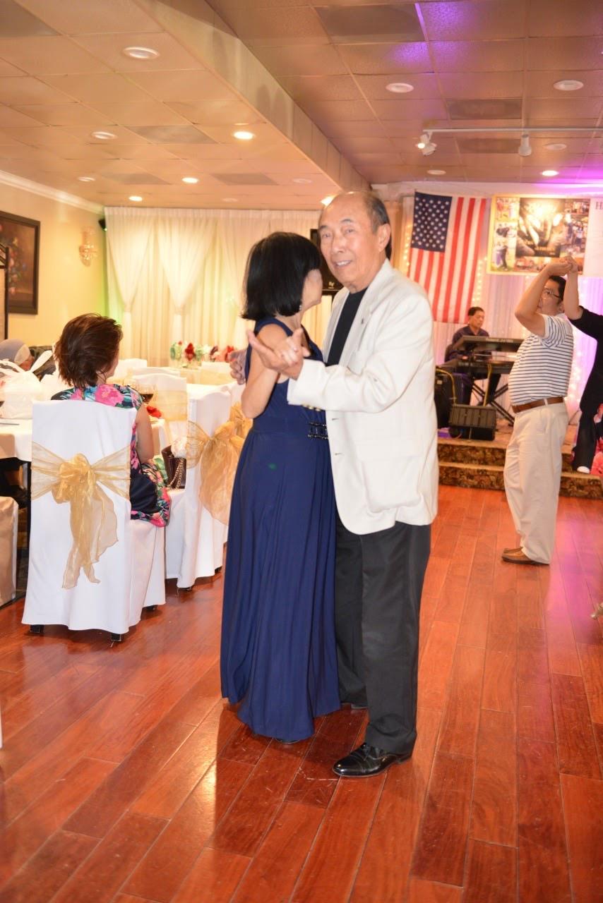 A couple enjoys dancing together at a vibrant celebration in a banquet hall.