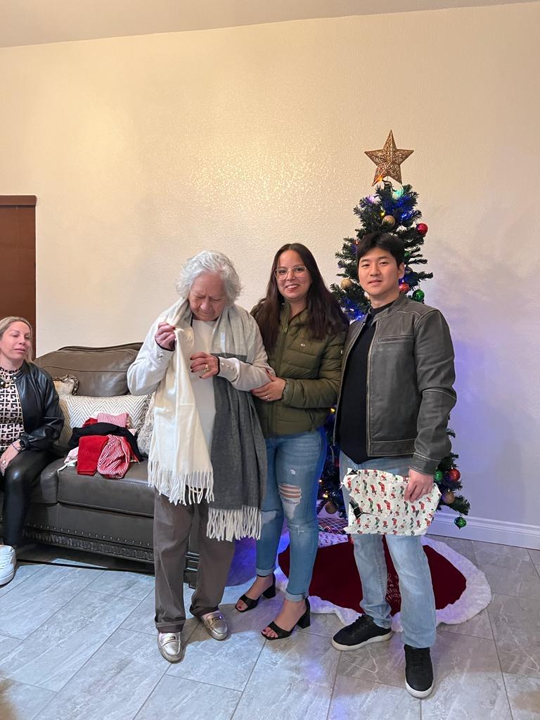 Three people pose happily near a Christmas tree while others relax nearby.