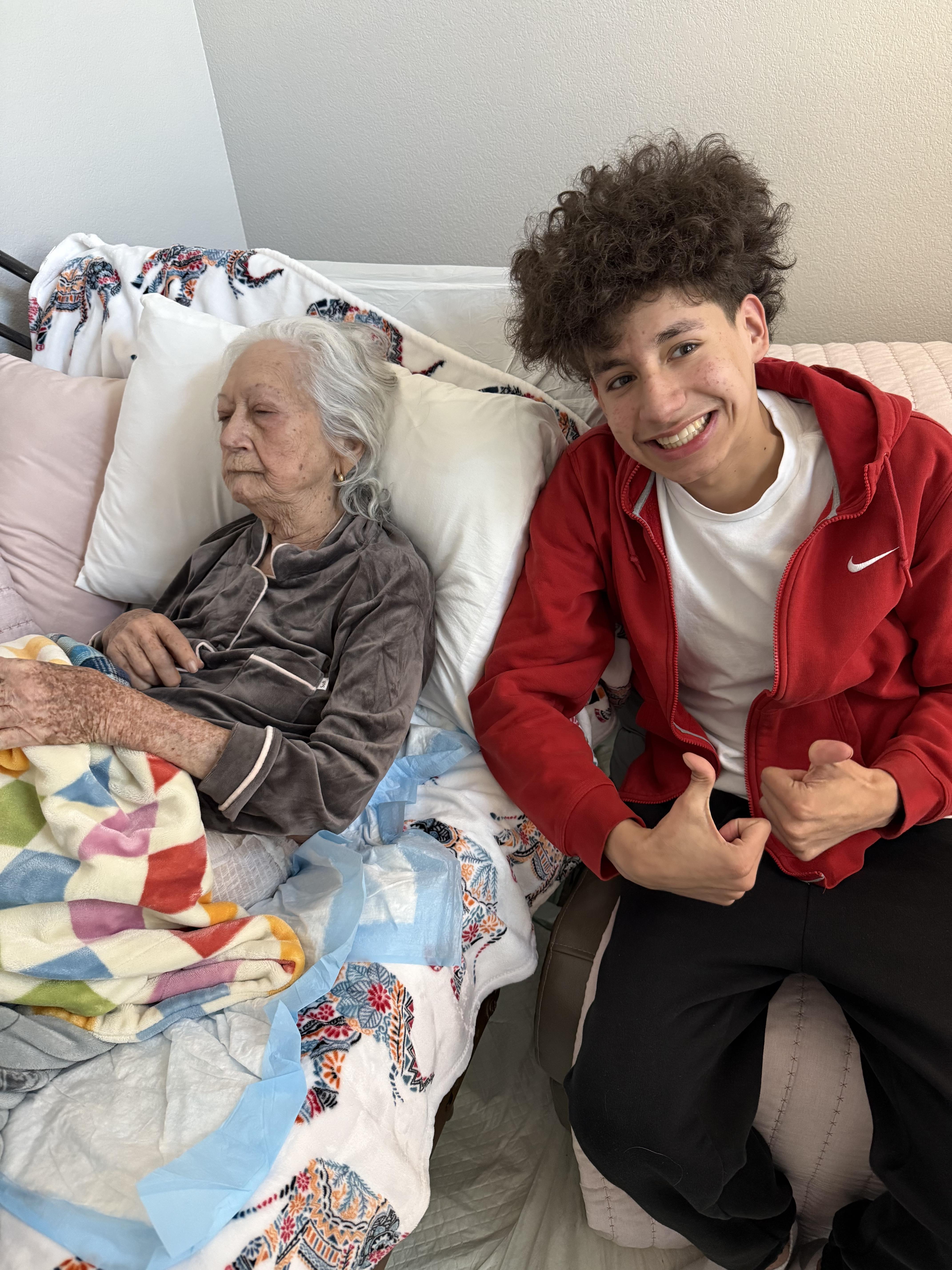 Young man shows a cheerful expression beside resting elderly woman in a cozy room.